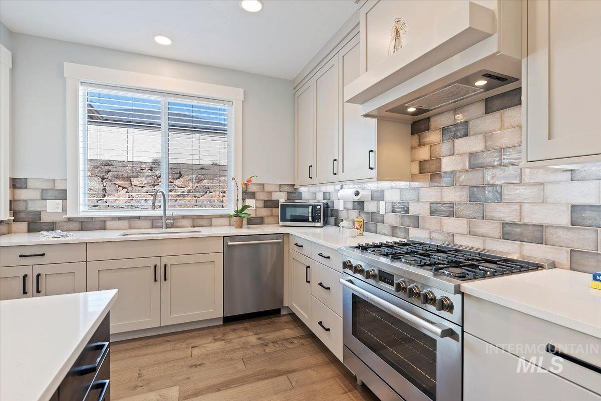 Kitchen with appliances with stainless steel finishes, premium range hood, light wood-style flooring, light stone countertops, and recessed lighting