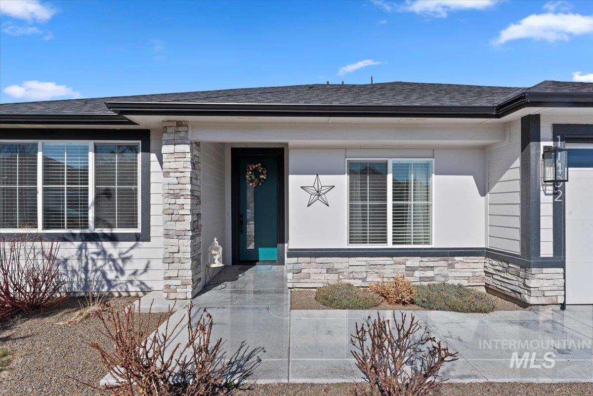 View of exterior entry featuring stone siding and a shingled roof