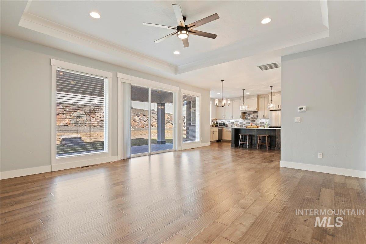 Unfurnished living room with a raised ceiling, dark wood-style flooring, a chandelier, recessed lighting, and ceiling fan
