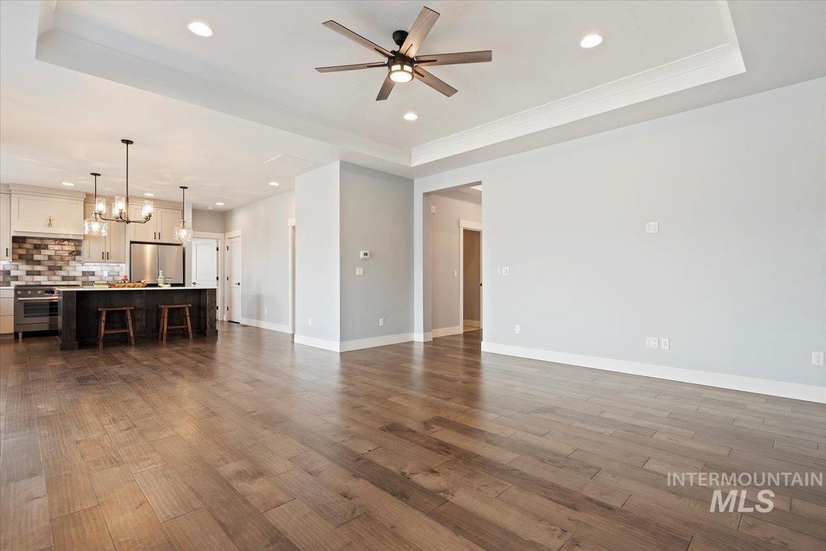 Unfurnished living room featuring a tray ceiling, recessed lighting, dark wood-type flooring, a ceiling fan, and a chandelier