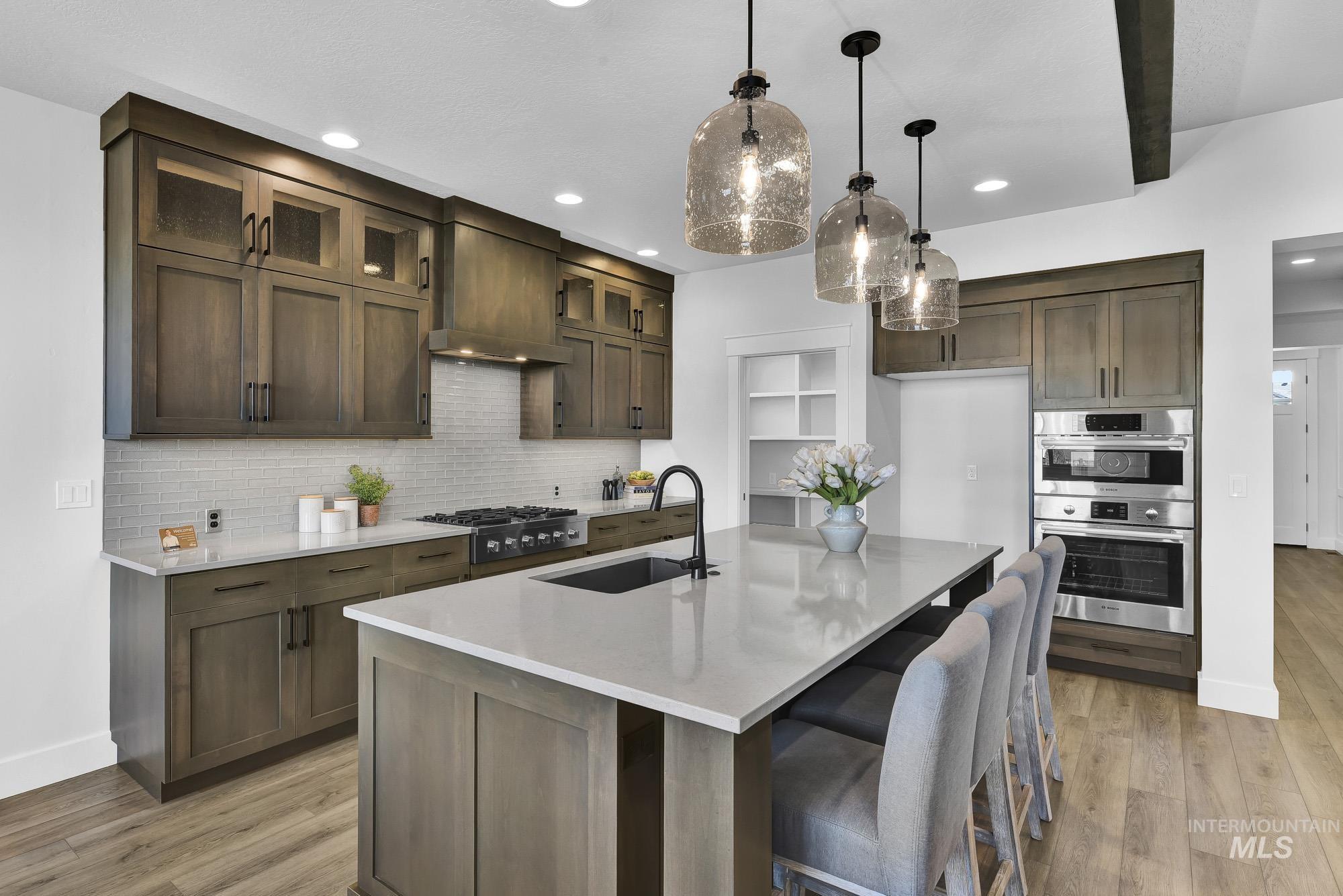 Kitchen featuring pendant lighting, light stone counters, backsplash, glass insert cabinets, and recessed lighting