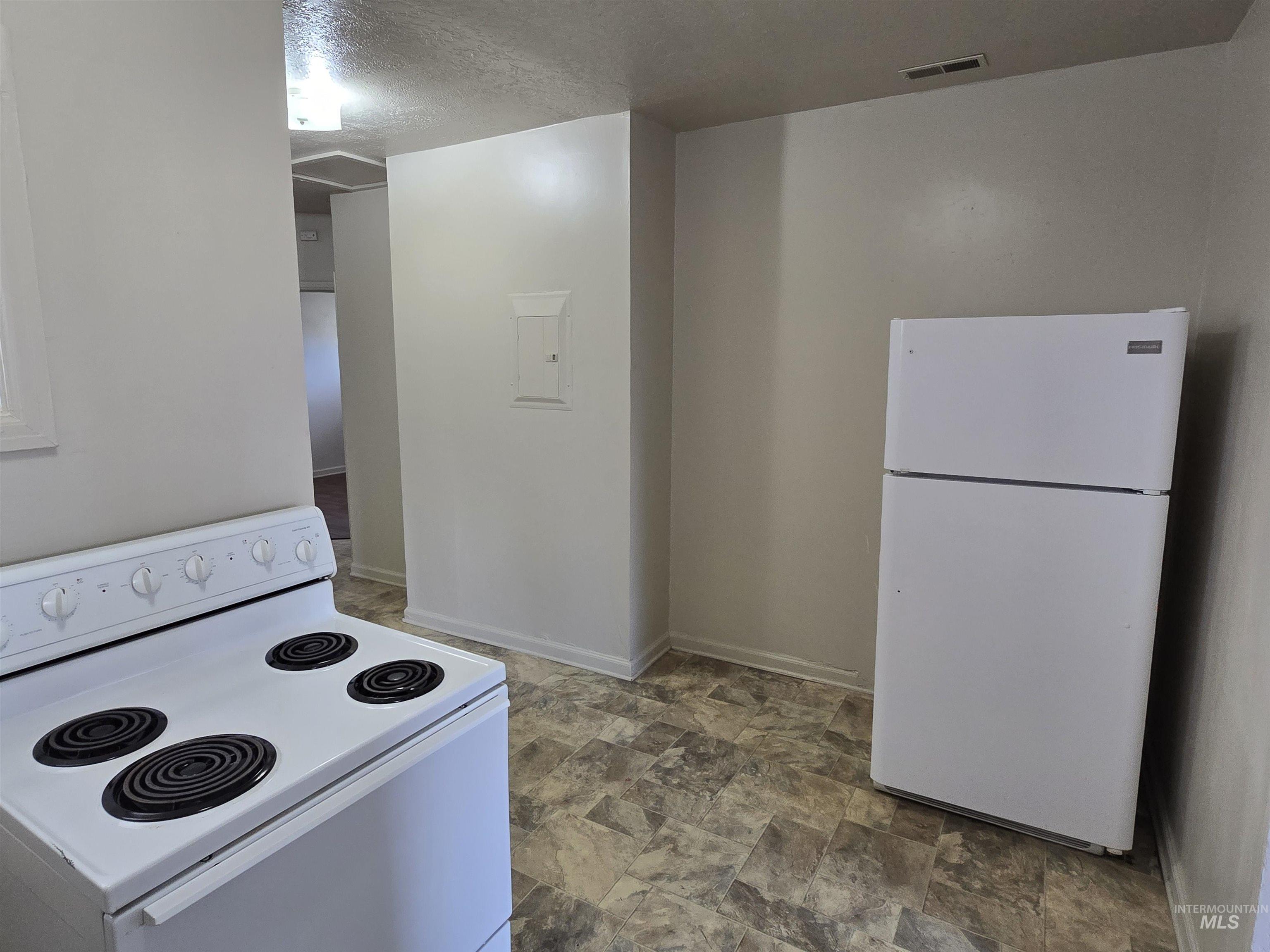Kitchen featuring white appliances, a textured ceiling, and stone finish flooring