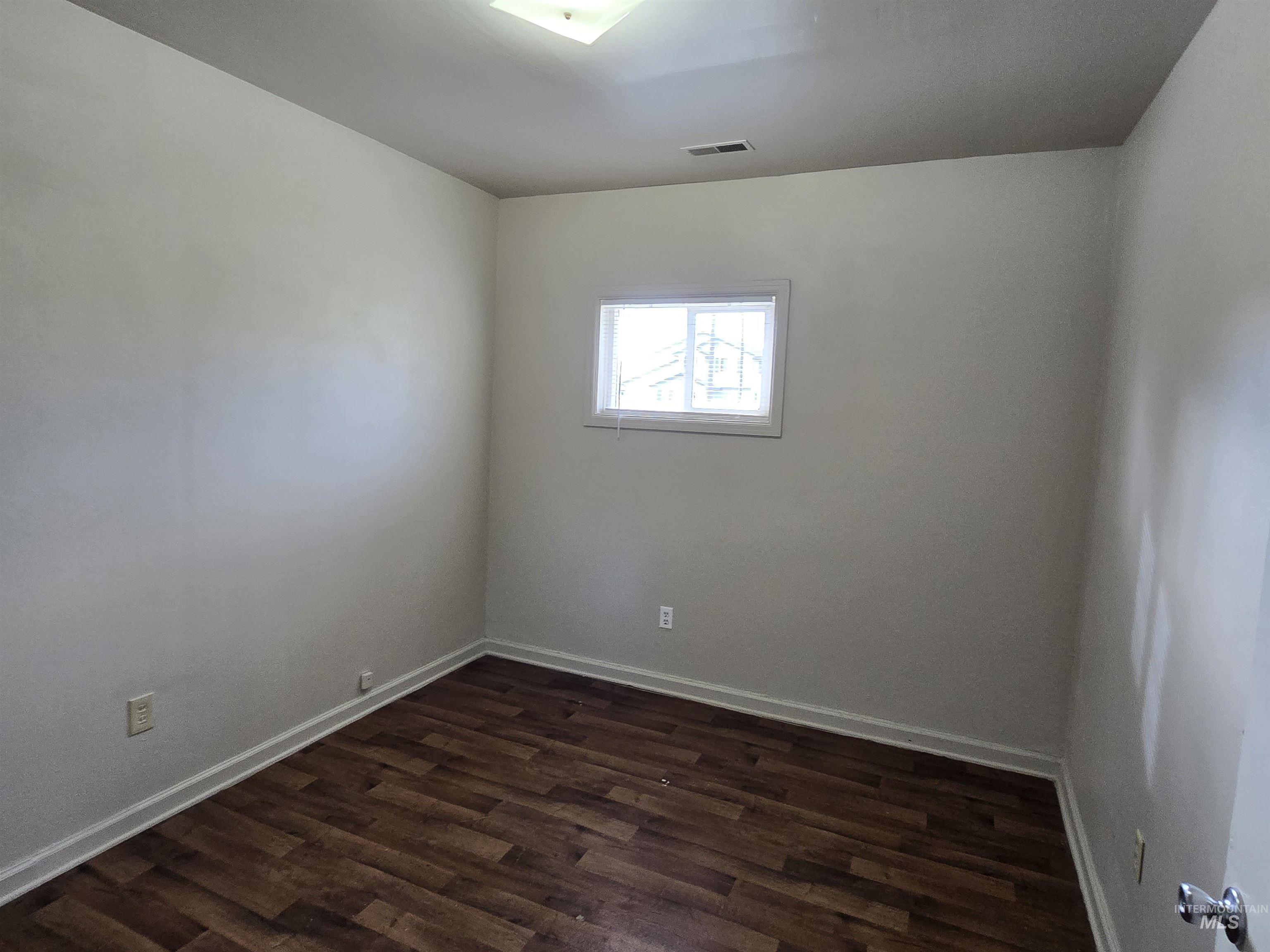 Spare room with dark wood-style floors and baseboards