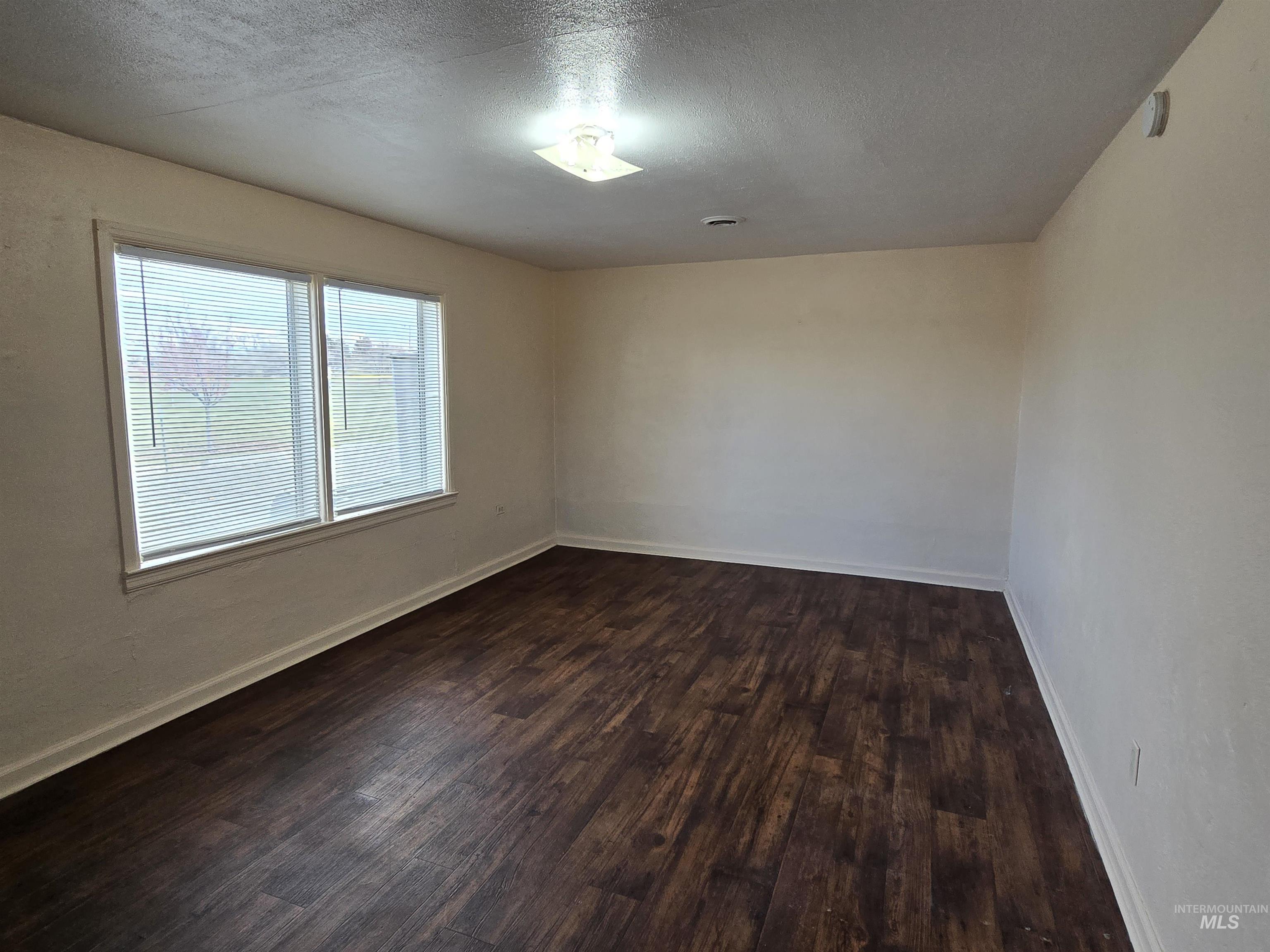 Empty room with a textured ceiling and dark wood-style flooring