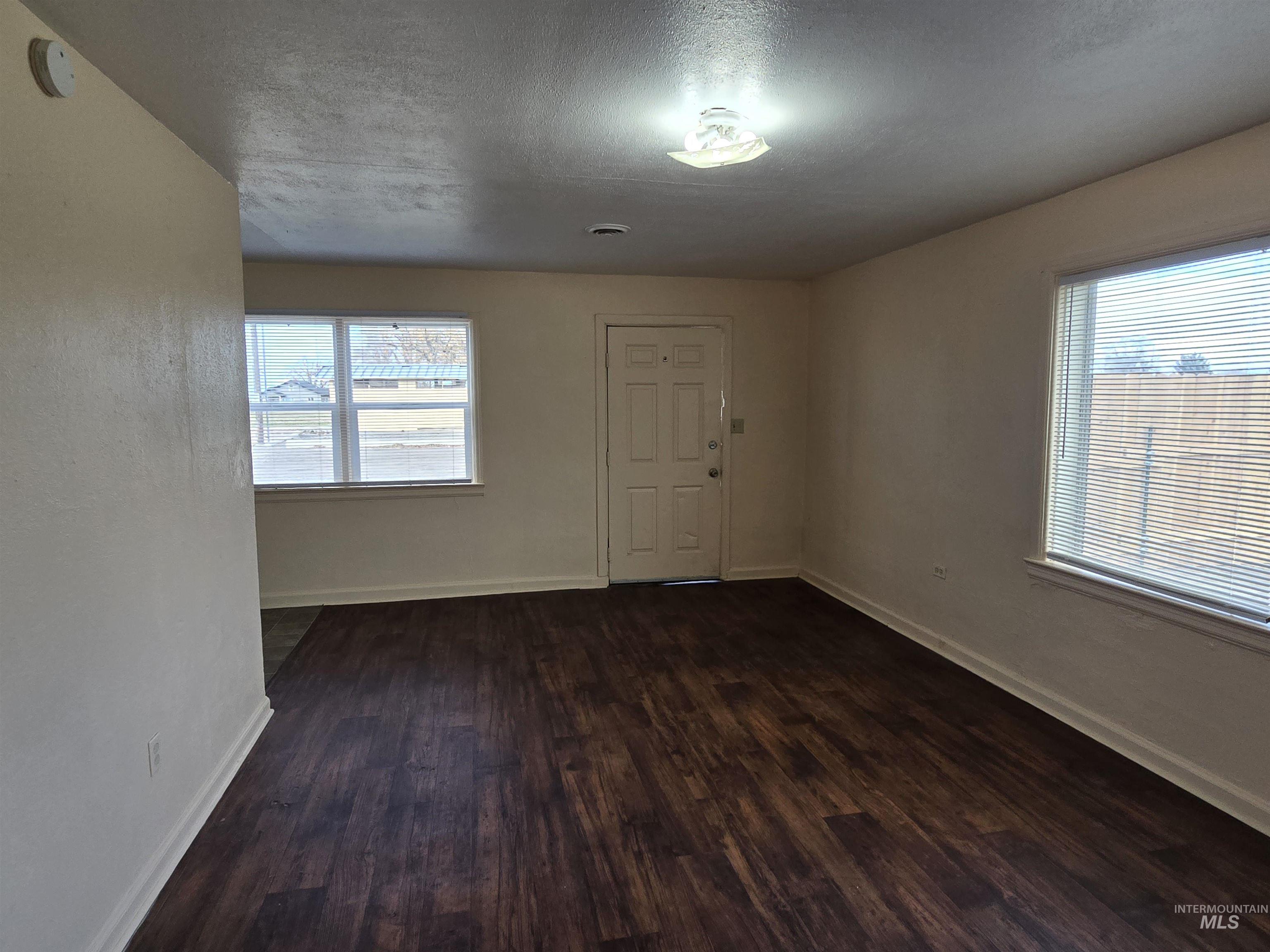 Empty room featuring a textured ceiling, plenty of natural light, and dark wood finished floors