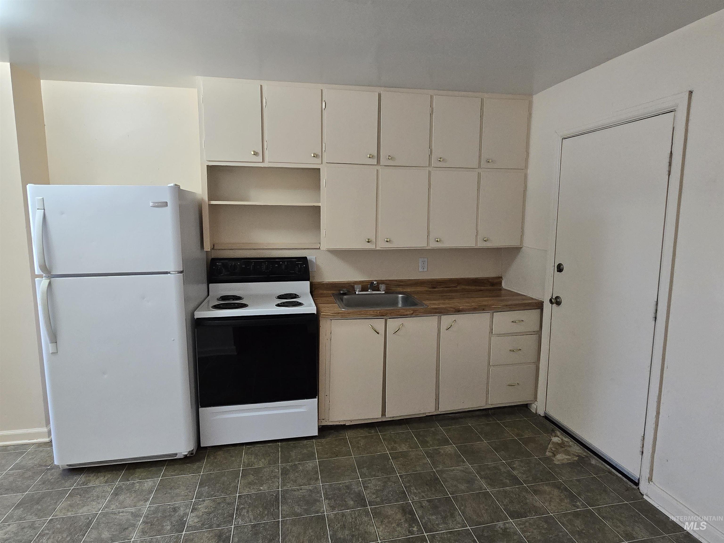 Kitchen with electric stove, freestanding refrigerator, open shelves, dark countertops, and white cabinetry