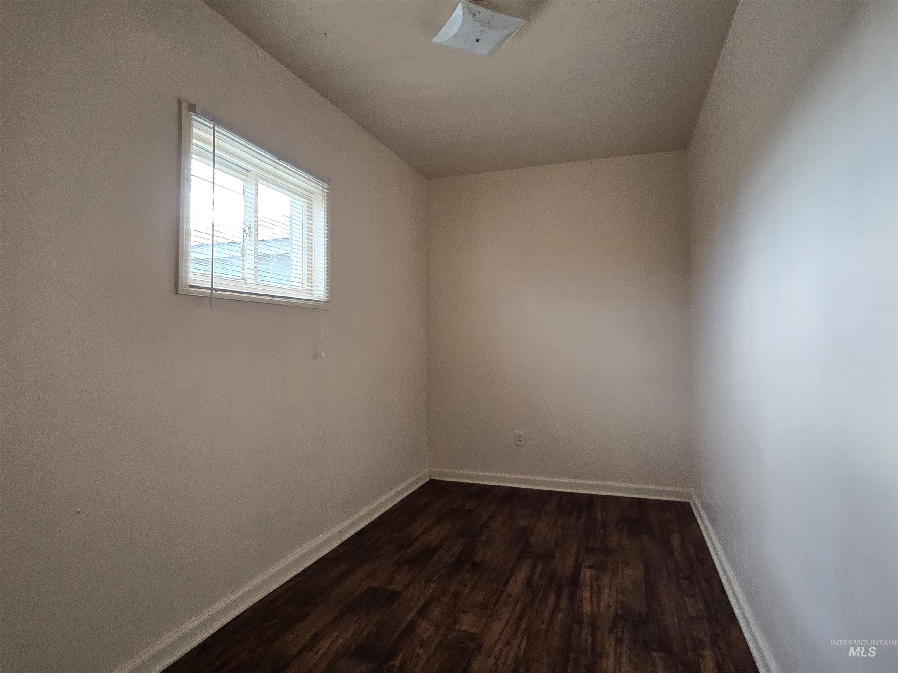 Spare room with dark wood-type flooring and baseboards