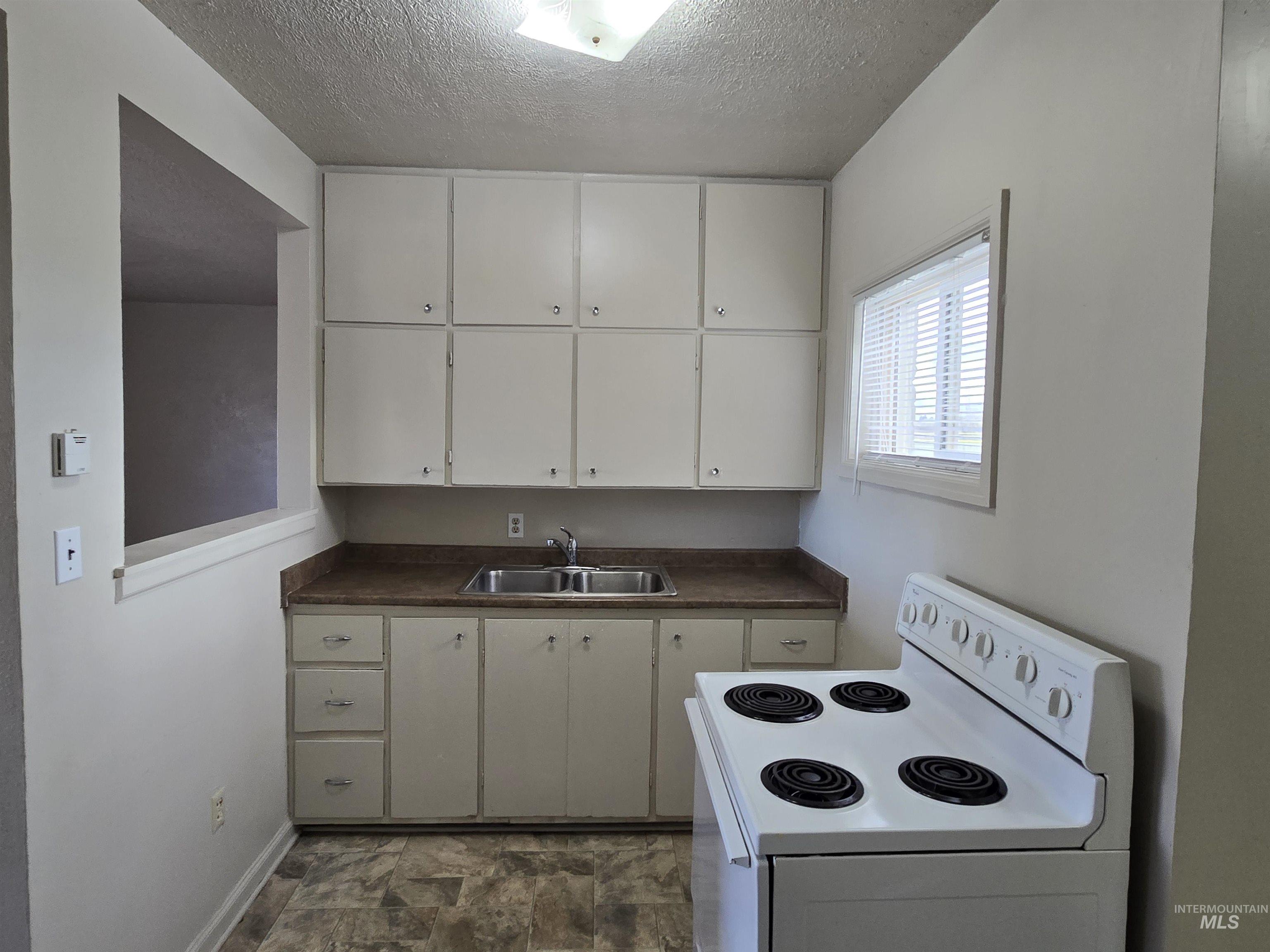 Kitchen featuring white electric range, dark countertops, white cabinetry, a textured ceiling, and stone finish floors