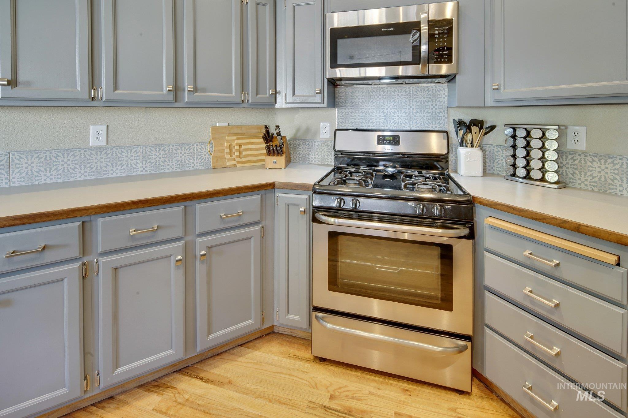 Kitchen with appliances with stainless steel finishes, light countertops, light wood-type flooring, gray cabinets, and backsplash