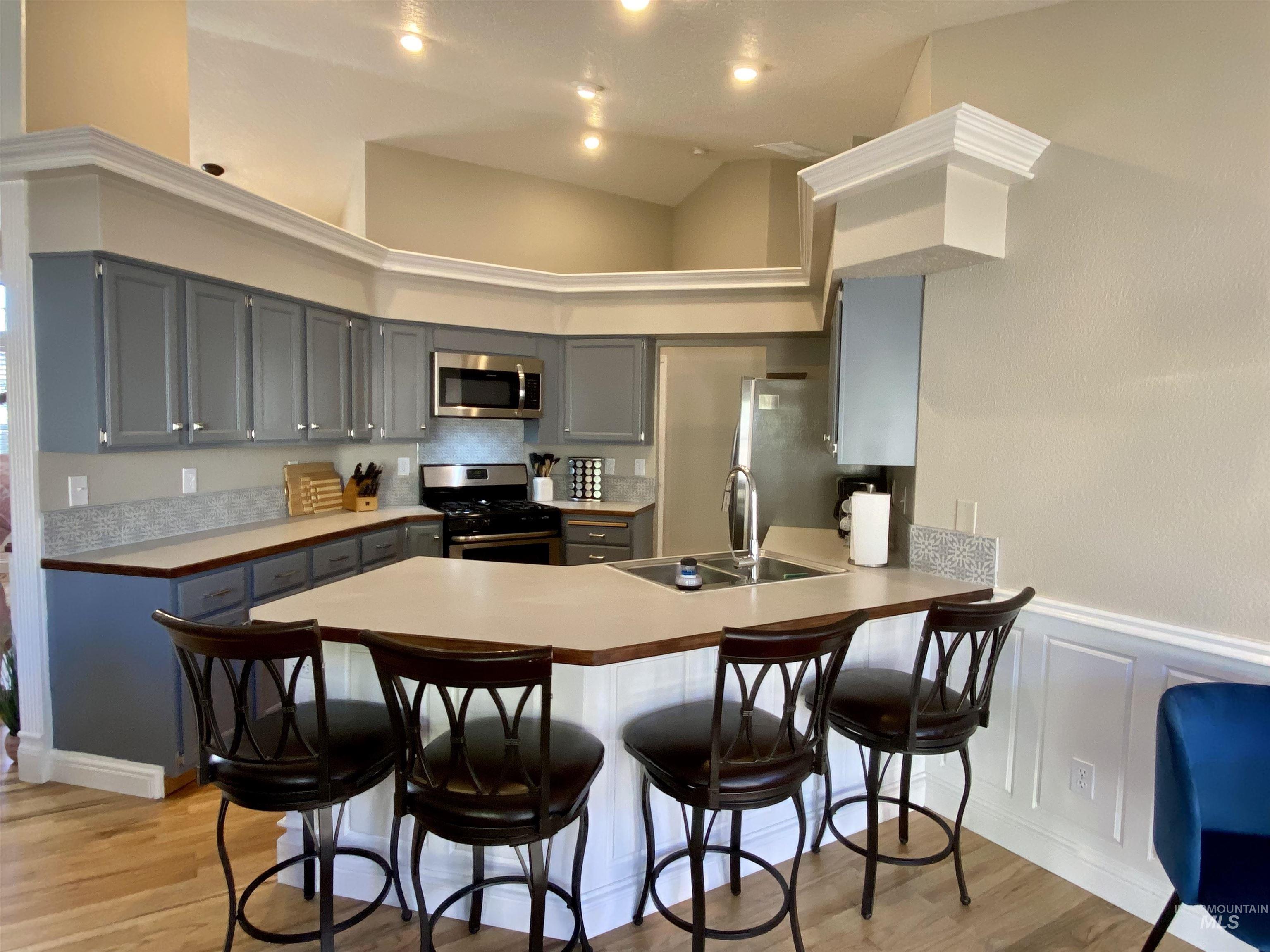 Kitchen featuring a kitchen bar, light wood-style flooring, stainless steel appliances, a high ceiling, and gray cabinetry