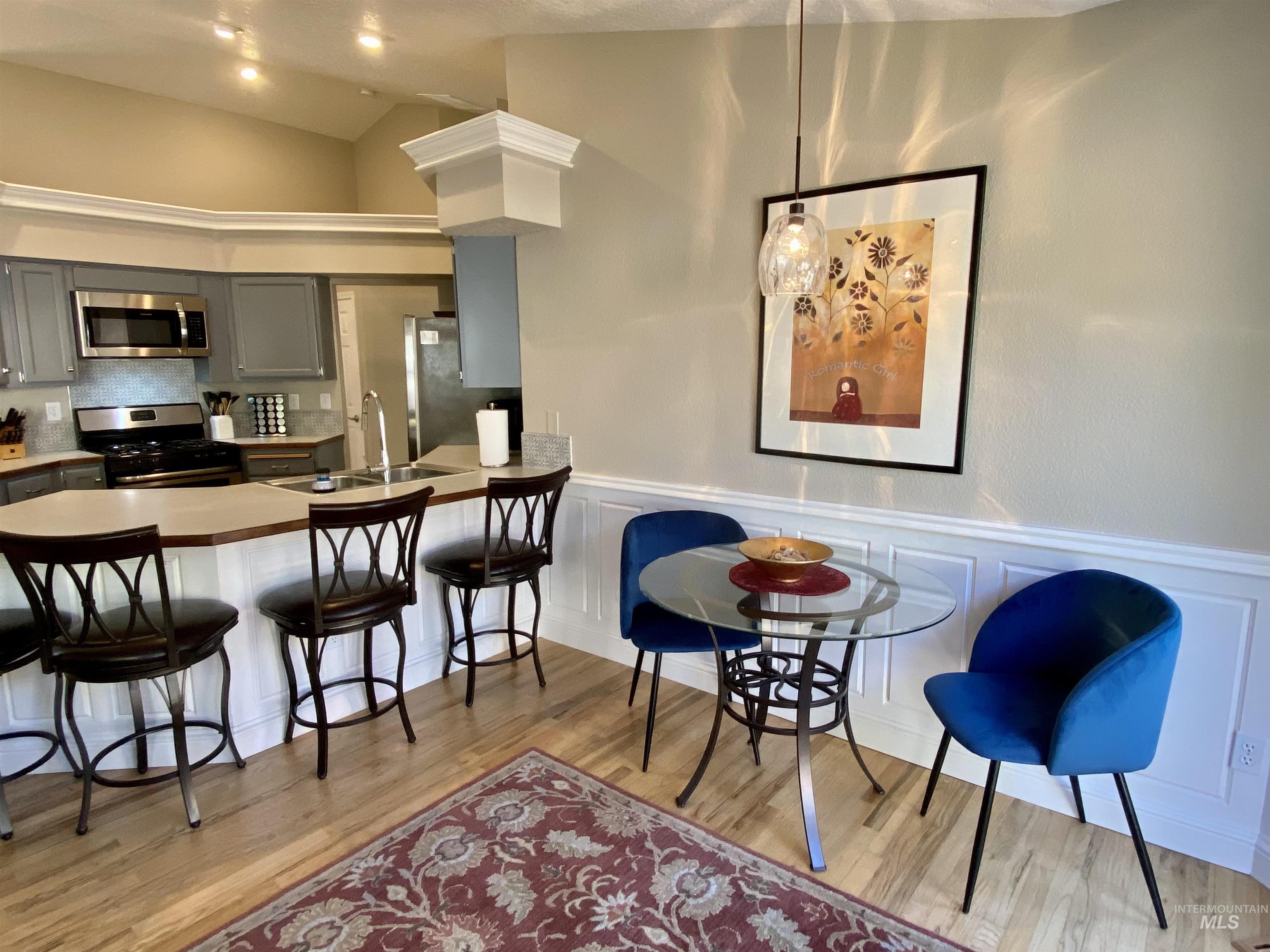 Kitchen with a breakfast bar, appliances with stainless steel finishes, gray cabinetry, light countertops, and light wood-type flooring