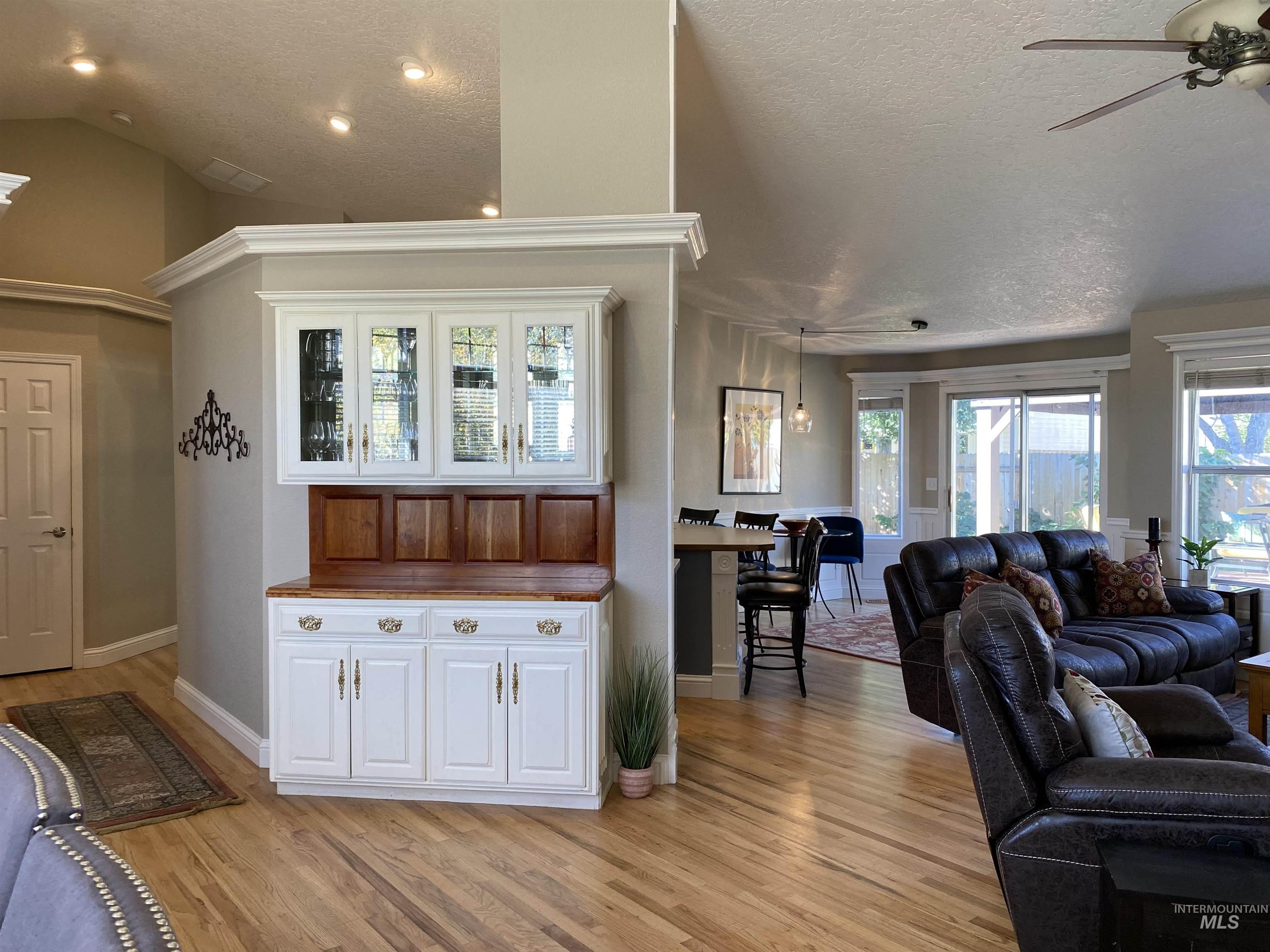 Living area featuring a textured ceiling, light wood finished floors, plenty of natural light, a ceiling fan, and vaulted ceiling