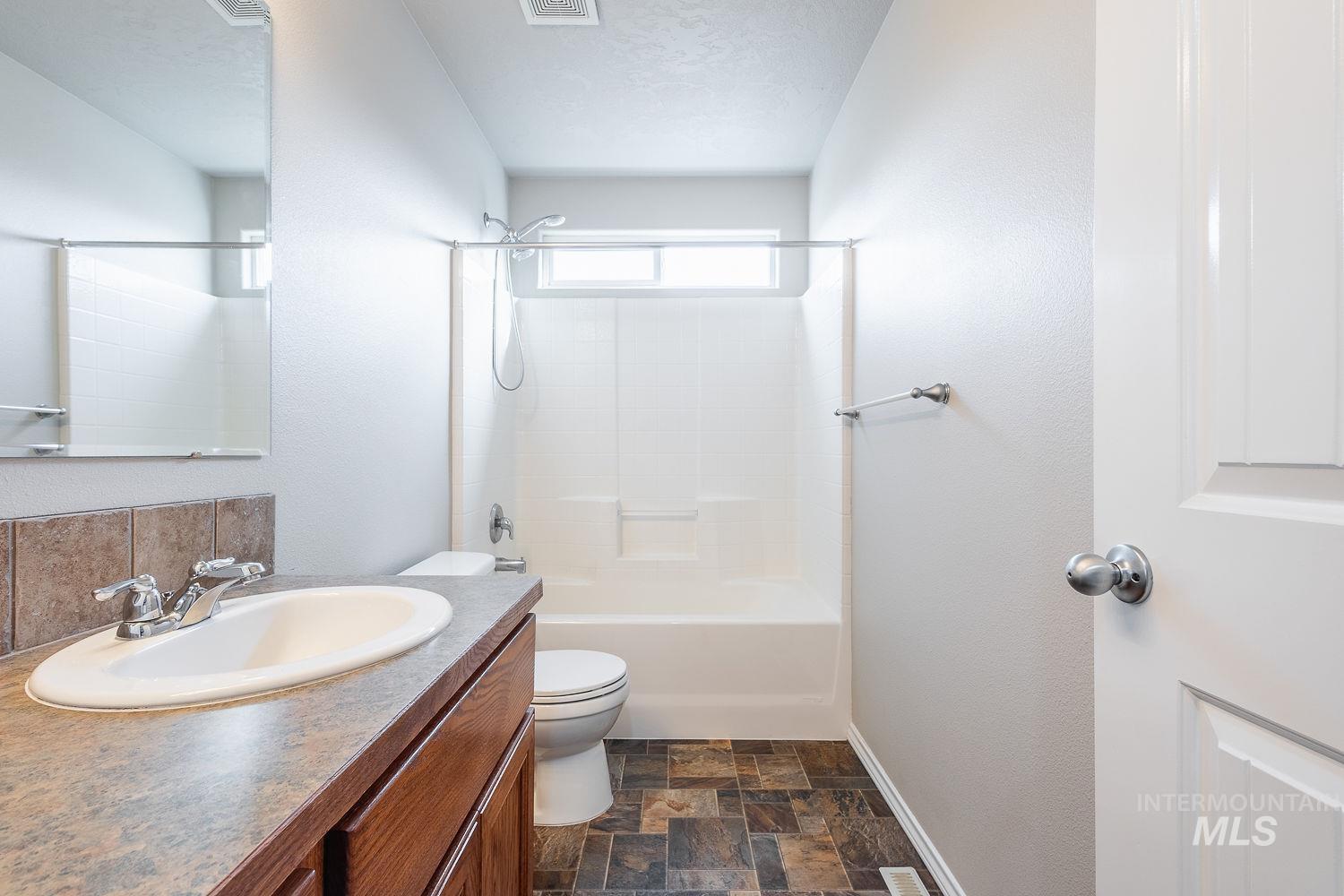 Full bath with vanity, stone finish floors,  shower combination, and a textured wall