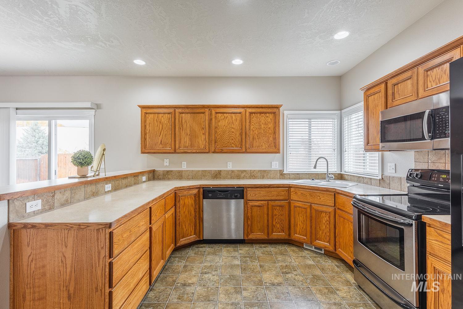 Kitchen featuring appliances with stainless steel finishes, light countertops, brown cabinetry, a peninsula, and a textured ceiling