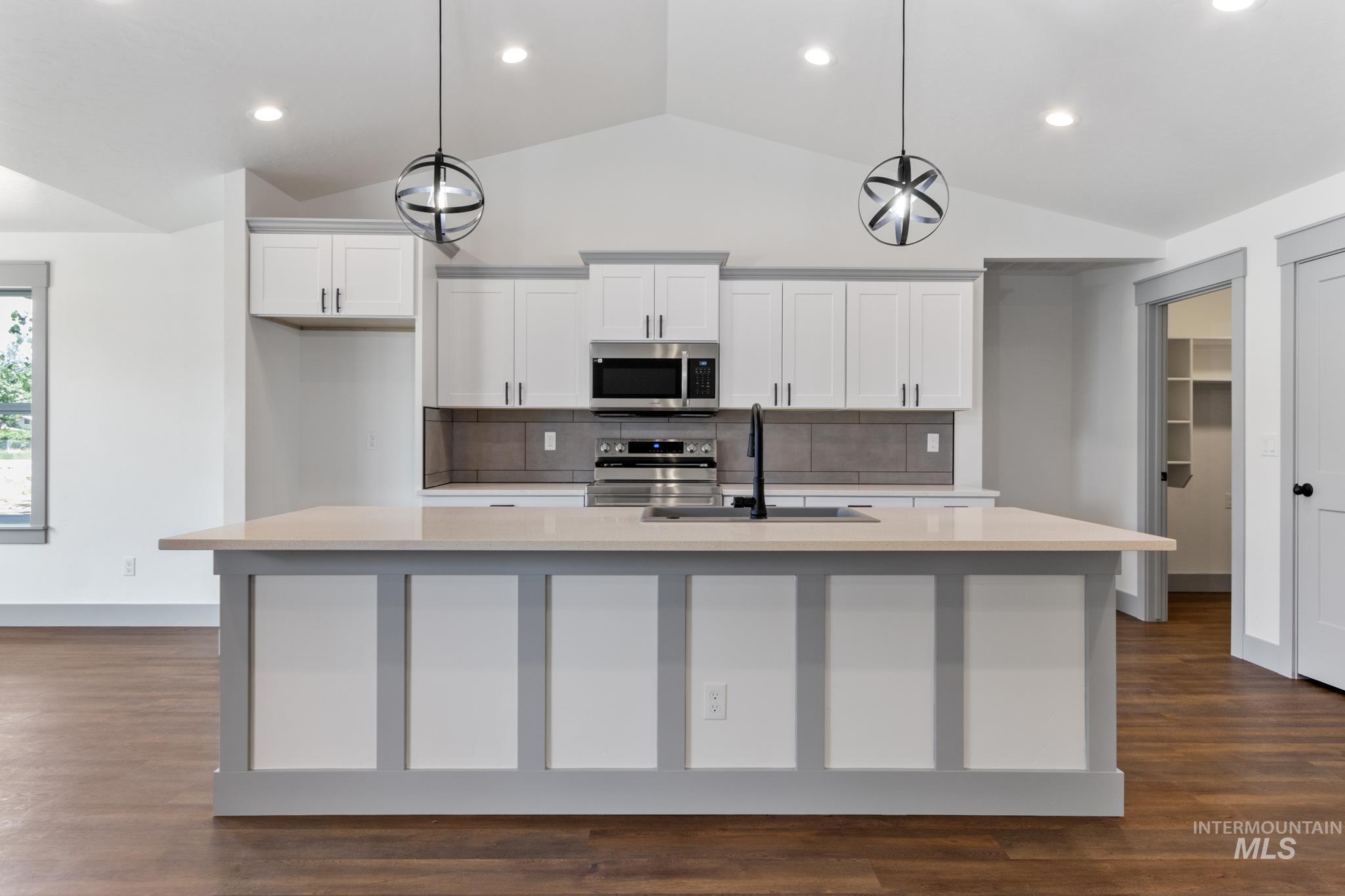 Kitchen with decorative backsplash, white cabinets, lofted ceiling, dark wood-type flooring, and stainless steel appliances