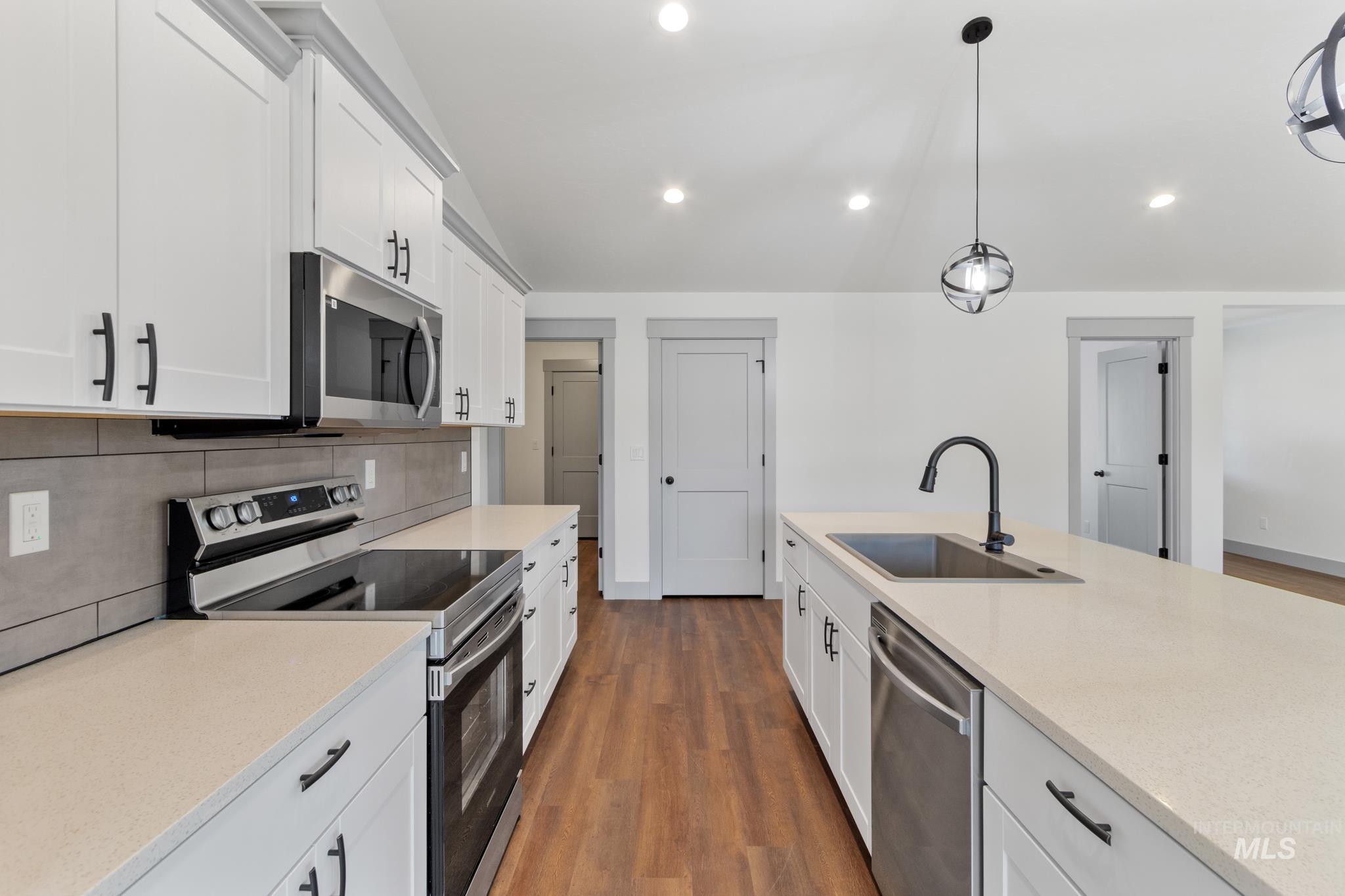 Kitchen with stainless steel appliances, dark wood-type flooring, white cabinetry, decorative backsplash, and recessed lighting