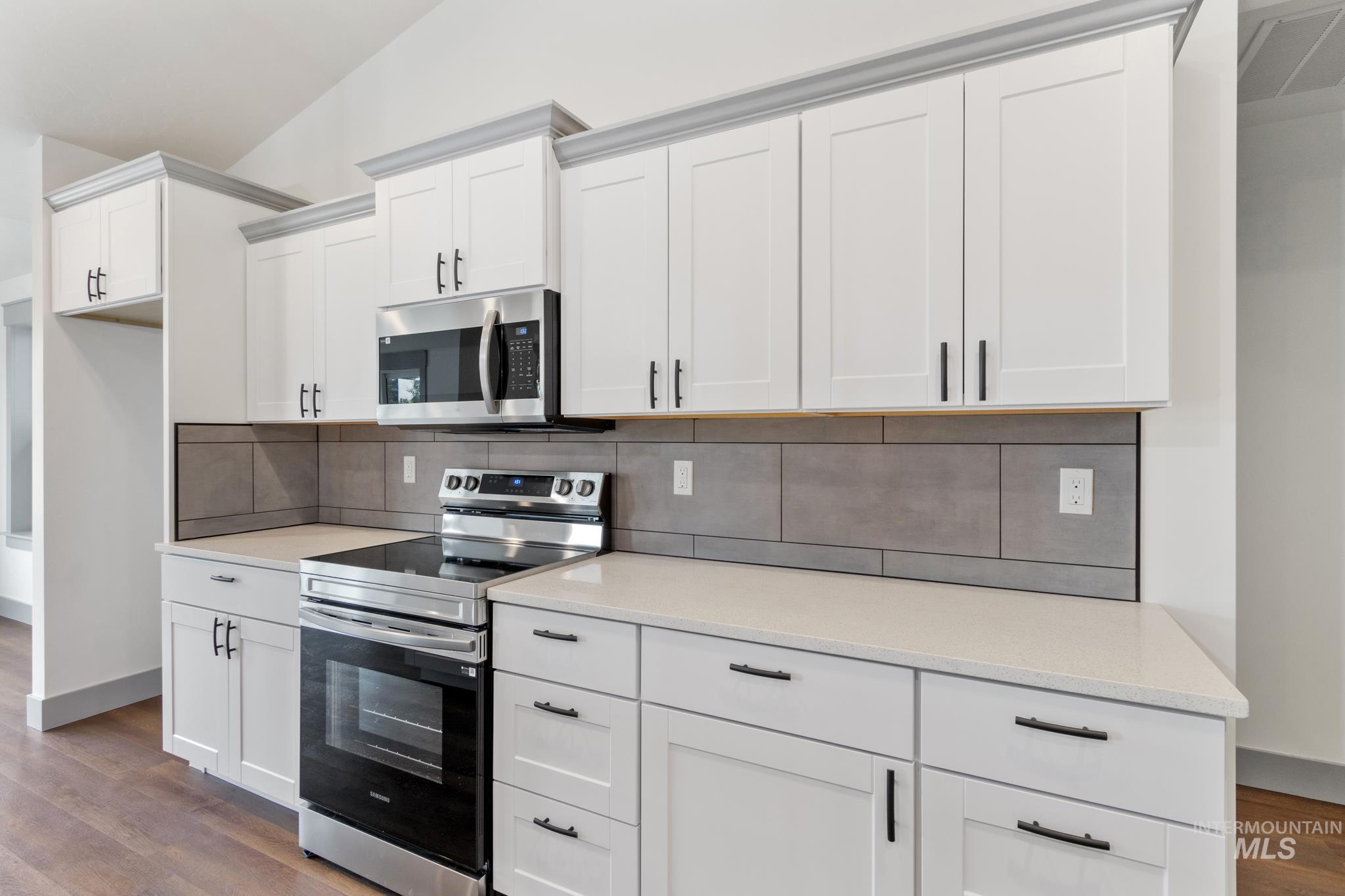 Kitchen featuring appliances with stainless steel finishes, white cabinetry, dark wood finished floors, decorative backsplash, and light stone counters