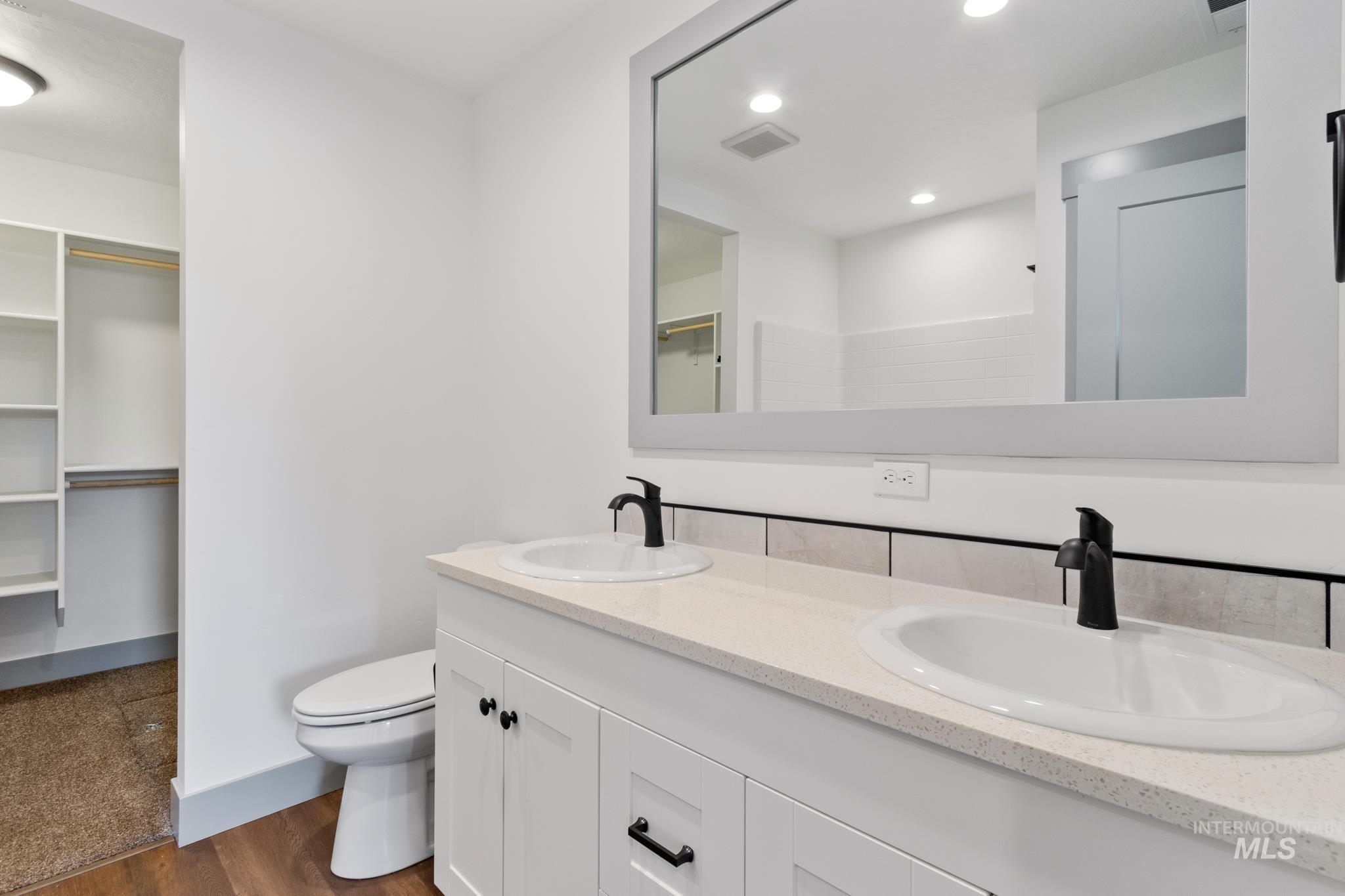 Full bath featuring a spacious closet, double vanity, dark wood-style flooring, and recessed lighting