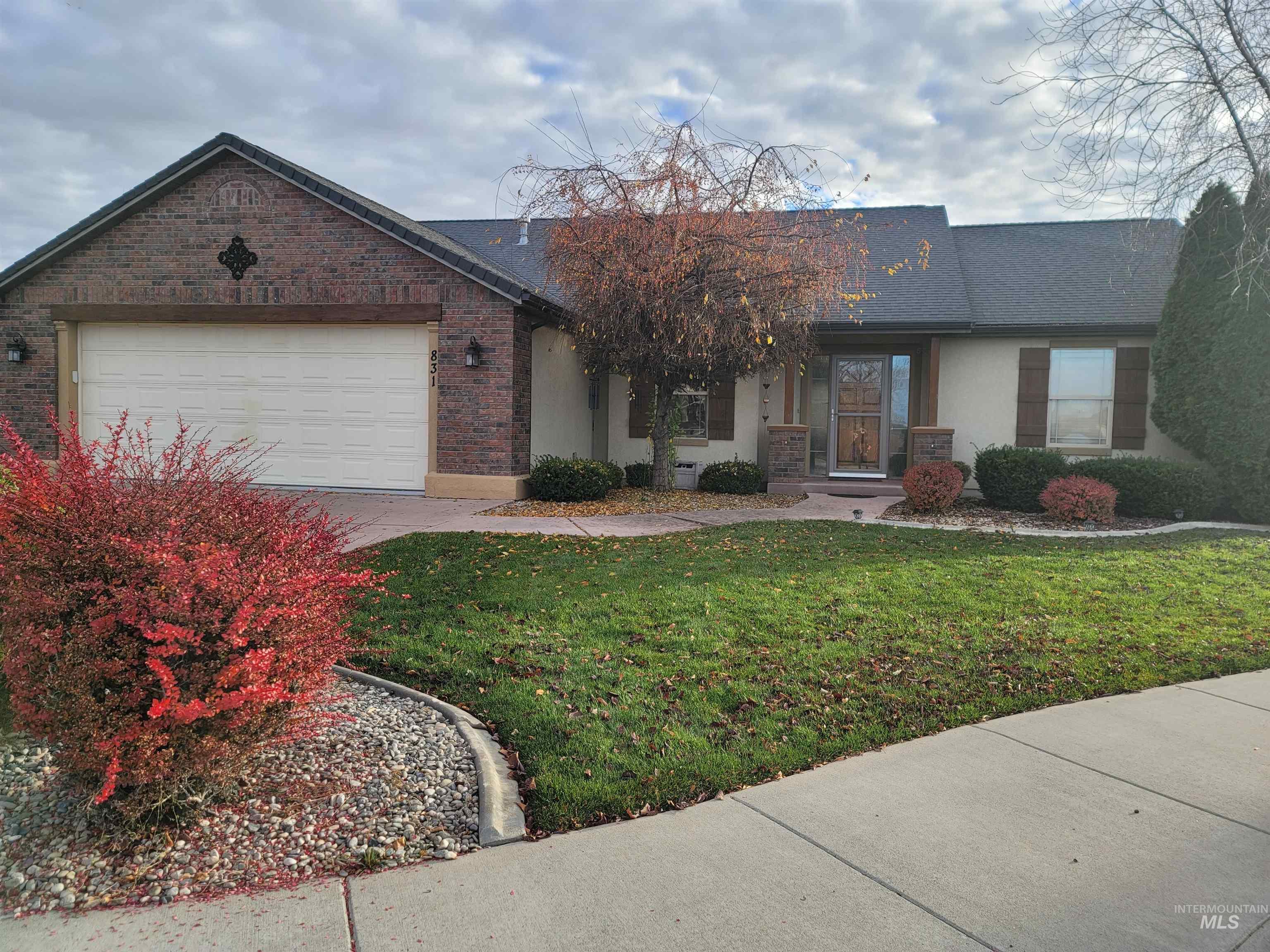 Ranch-style home with stucco siding, a front yard, brick siding, a garage, and a shingled roof