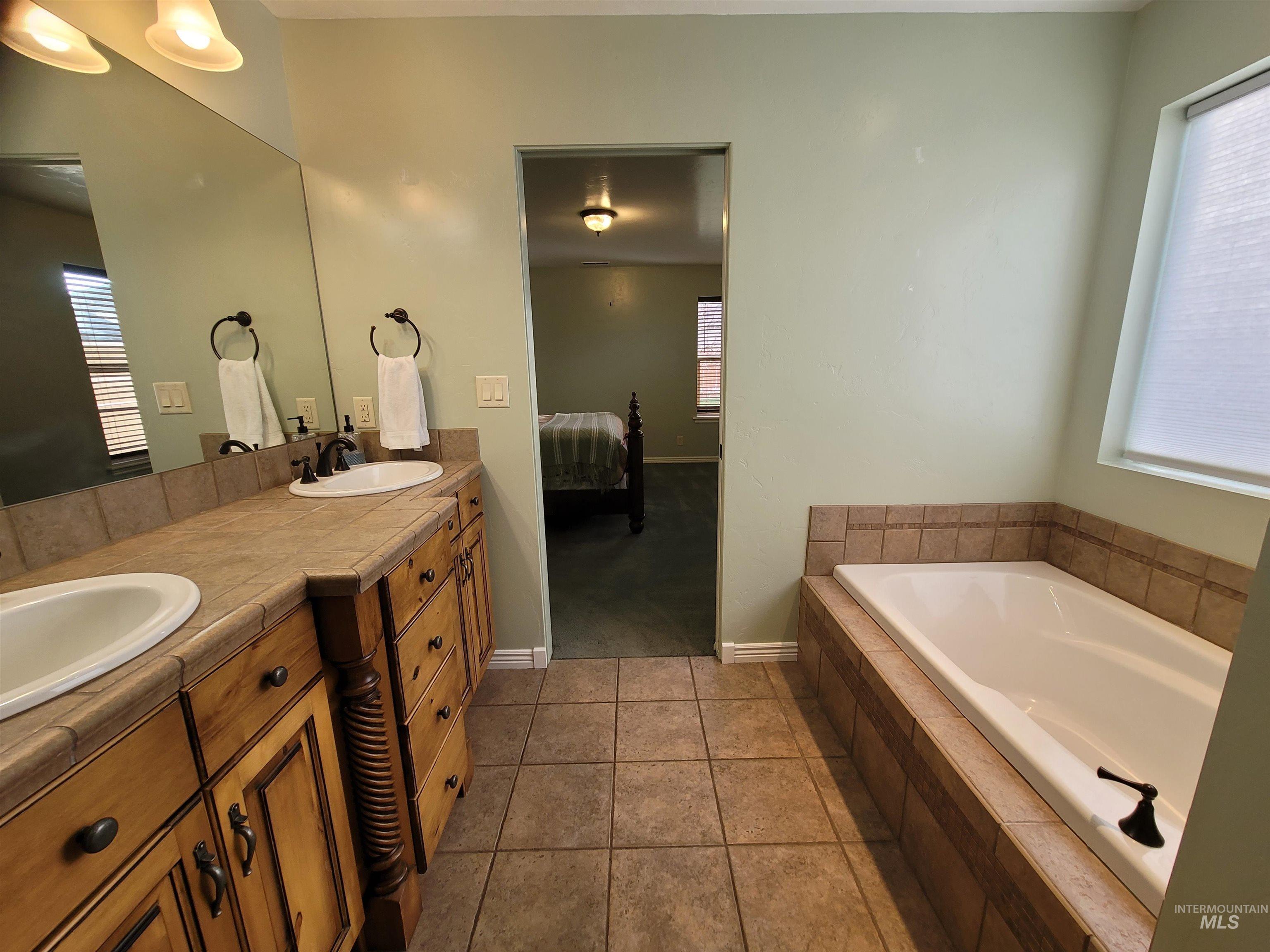 Ensuite bathroom featuring healthy amount of natural light, a garden tub, double vanity, and light tile patterned floors