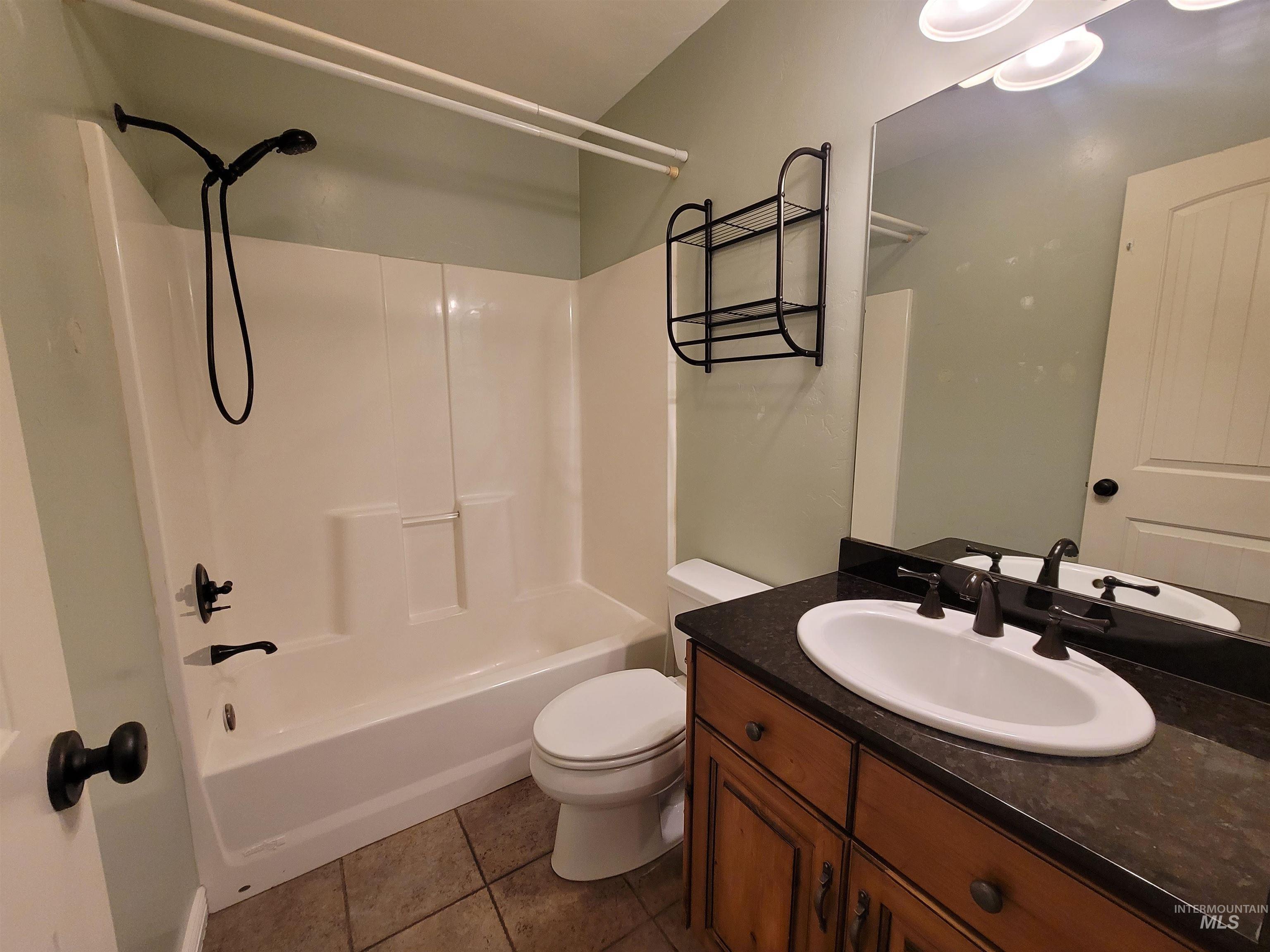 Bathroom with vanity, washtub / shower combination, and dark tile patterned flooring