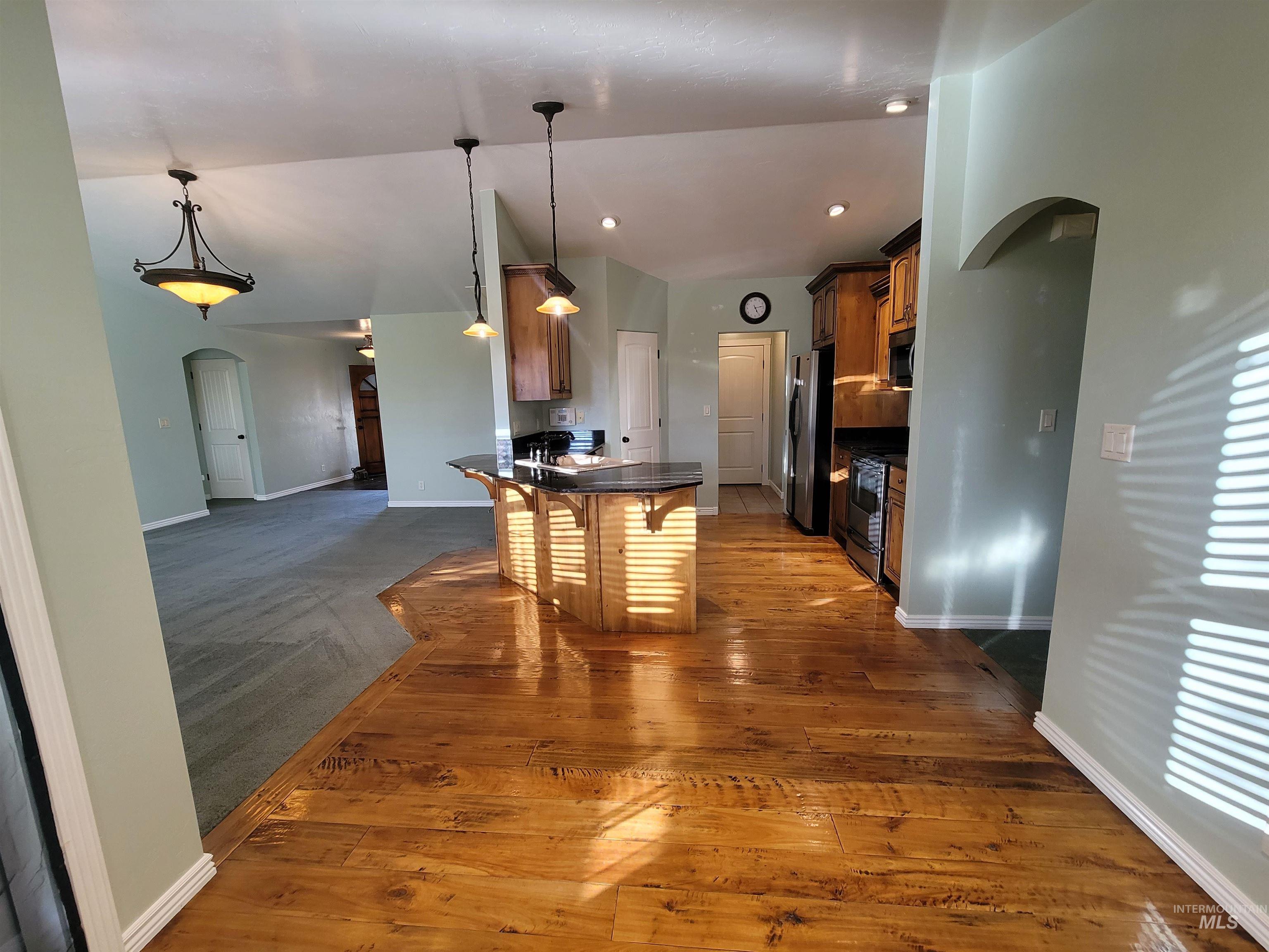 Kitchen featuring dark countertops, arched walkways, dark wood-style floors, a breakfast bar, and appliances with stainless steel finishes
