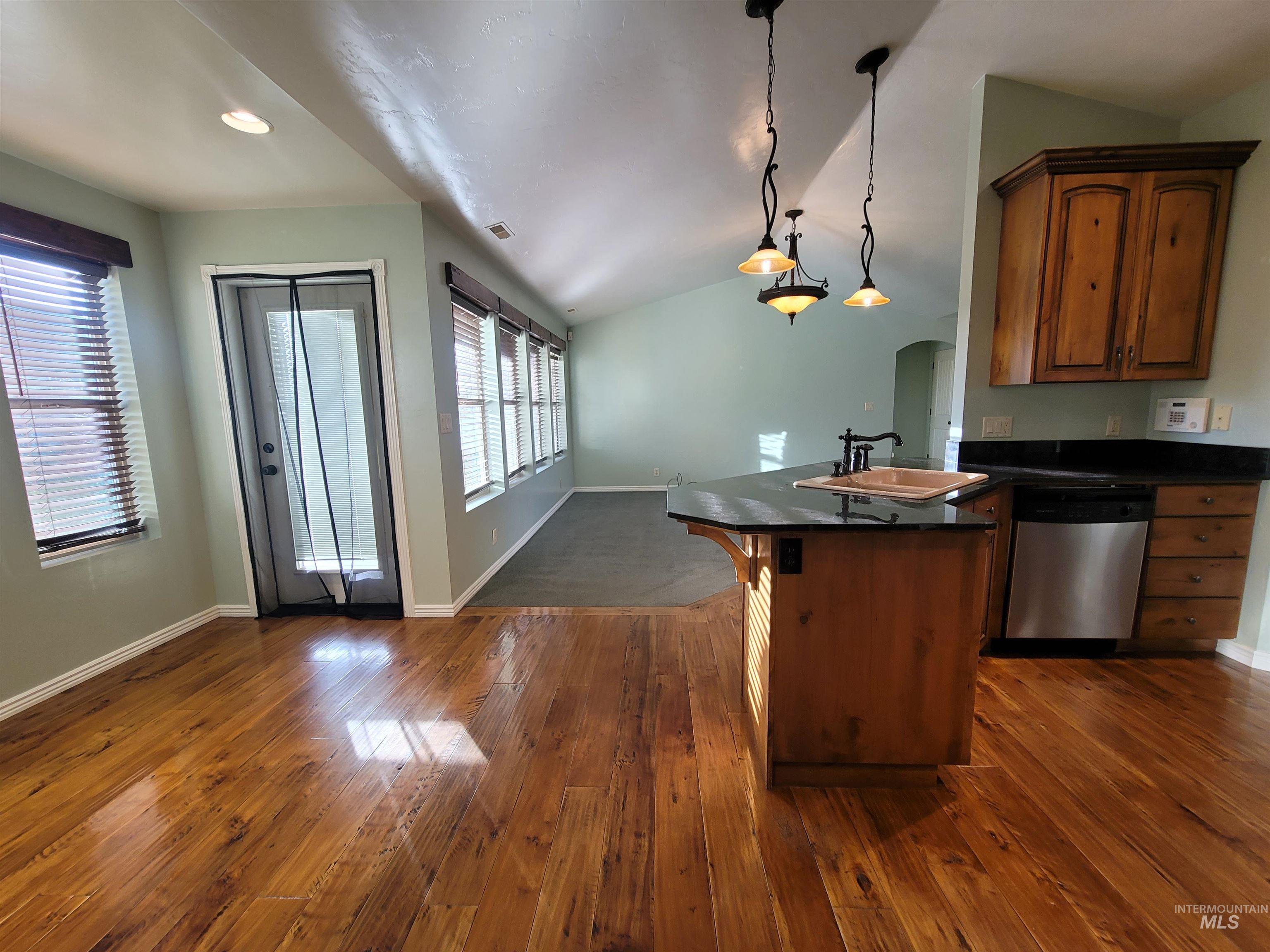 Kitchen featuring vaulted ceiling, dishwasher, a kitchen breakfast bar, dark wood-style floors, and hanging light fixtures