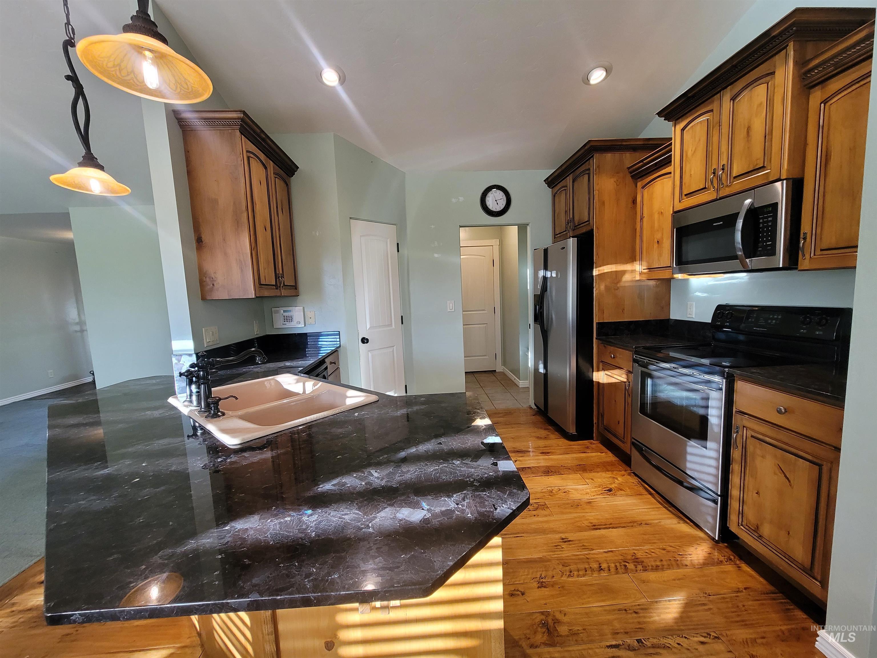 Kitchen featuring appliances with stainless steel finishes, a peninsula, brown cabinetry, dark stone counters, and recessed lighting