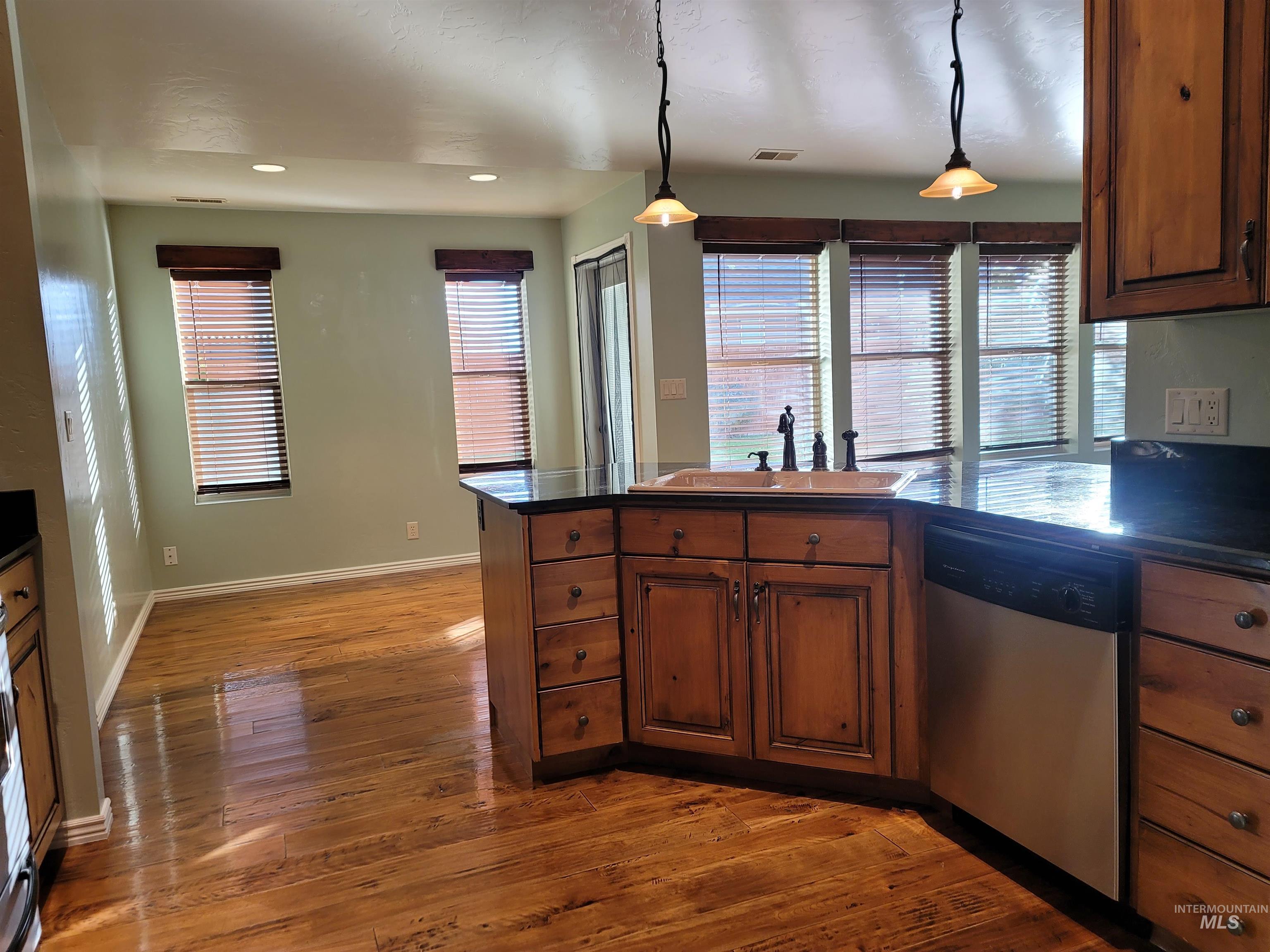 Kitchen with a peninsula, stainless steel dishwasher, dark wood-type flooring, hanging light fixtures, and recessed lighting
