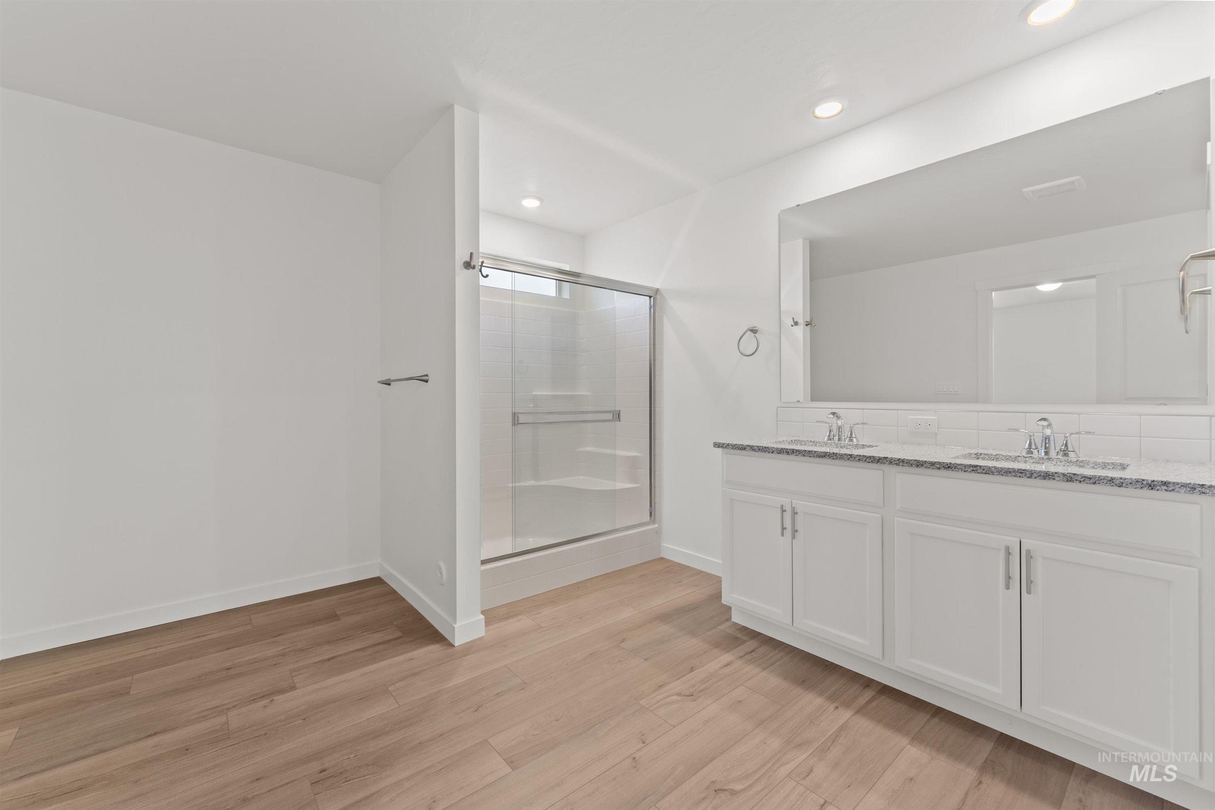 Bathroom featuring double vanity, a stall shower, light wood-type flooring, and recessed lighting