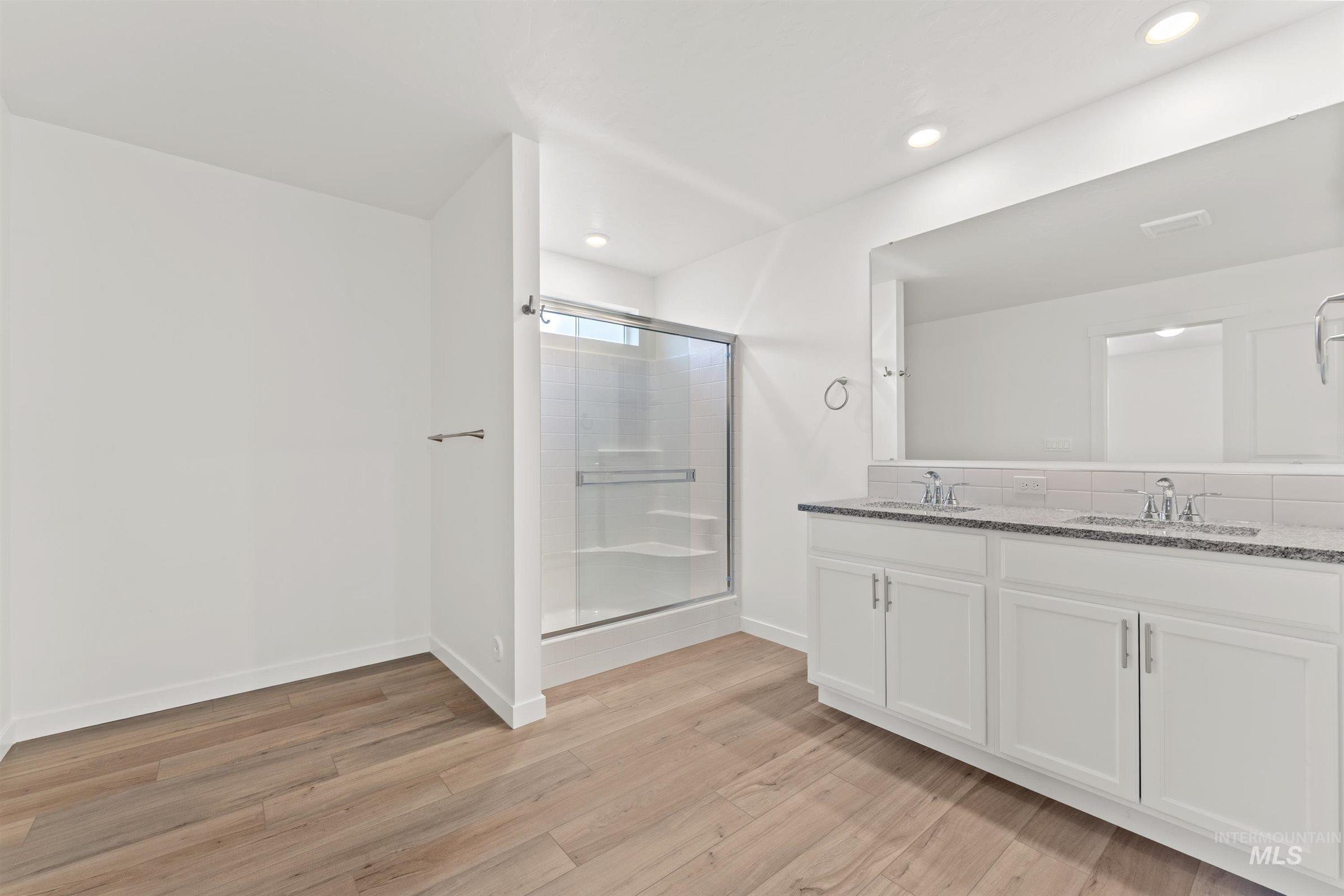 Bathroom with double vanity, light wood-style flooring, a stall shower, and recessed lighting