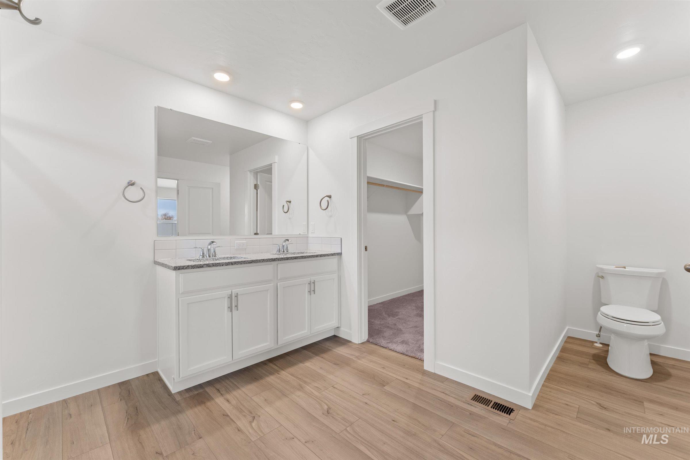 Bathroom featuring double vanity, light wood-style floors, a walk in closet, recessed lighting, and decorative backsplash