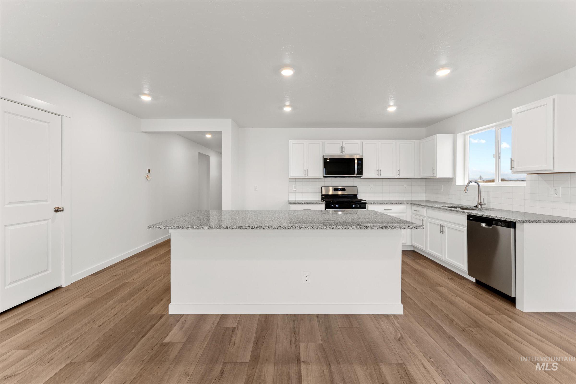 Kitchen with backsplash, white cabinets, light wood finished floors, stainless steel appliances, and recessed lighting