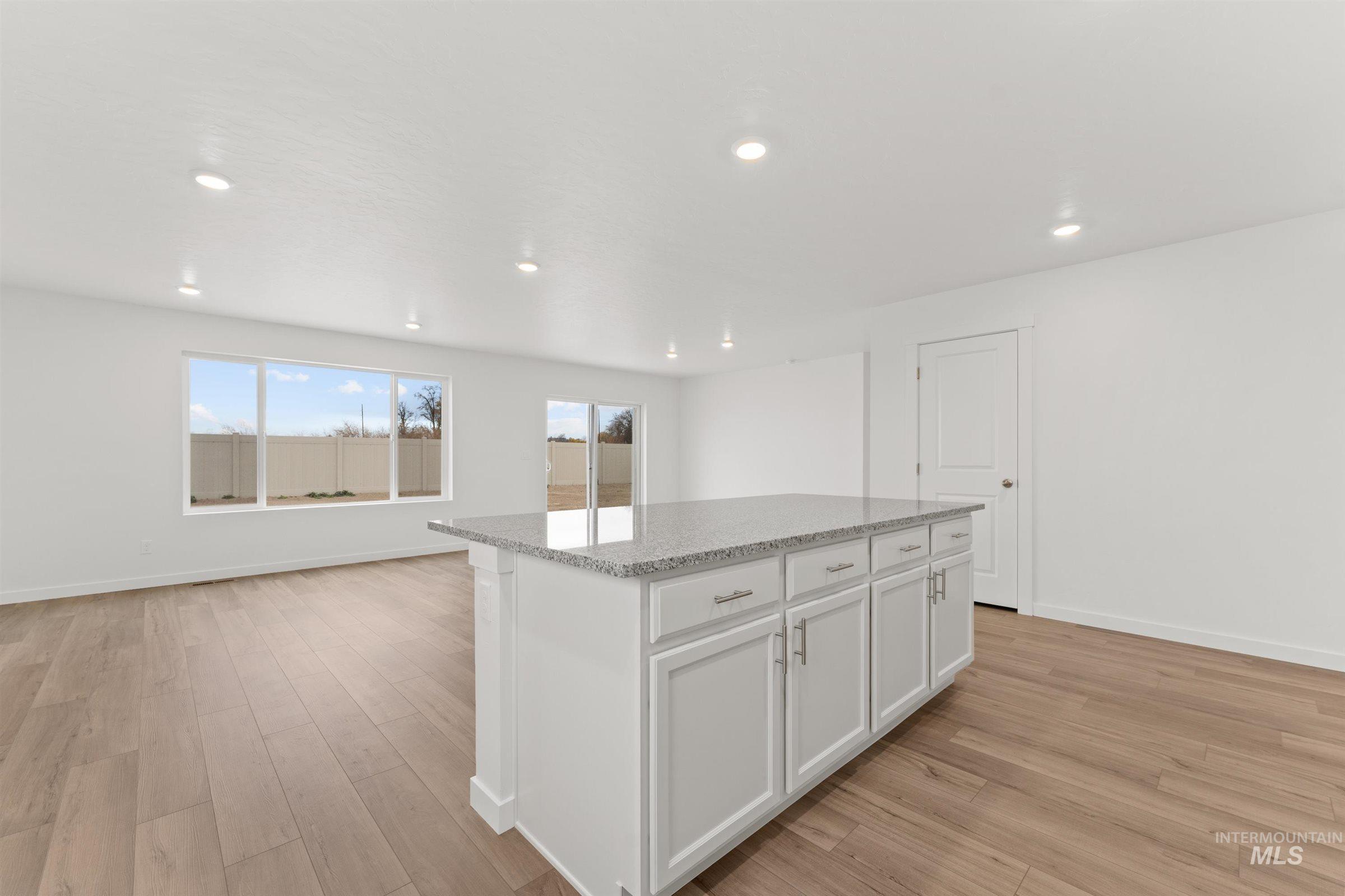 Kitchen featuring light stone counters, white cabinets, recessed lighting, light wood finished floors, and a center island
