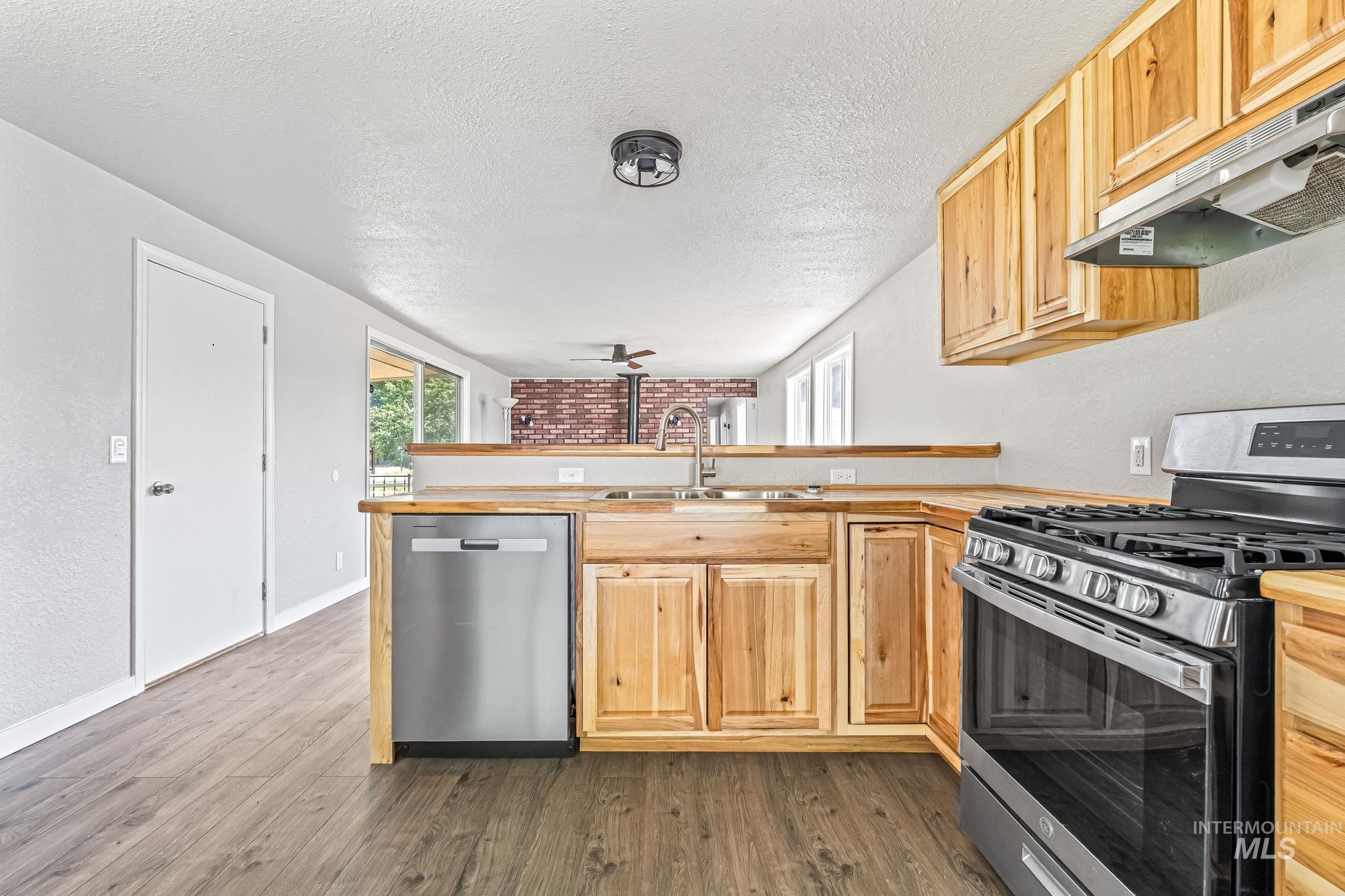Kitchen featuring stainless steel appliances, under cabinet range hood, a peninsula, dark wood-style flooring, and a textured ceiling