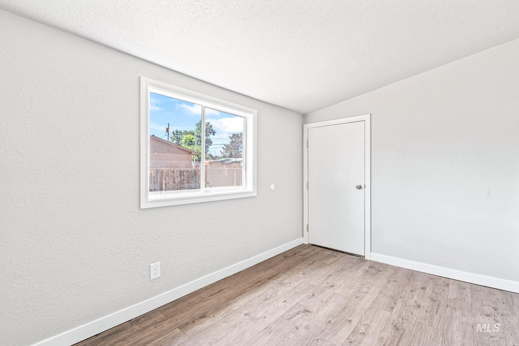 Unfurnished room featuring light wood-type flooring, lofted ceiling, and a textured ceiling