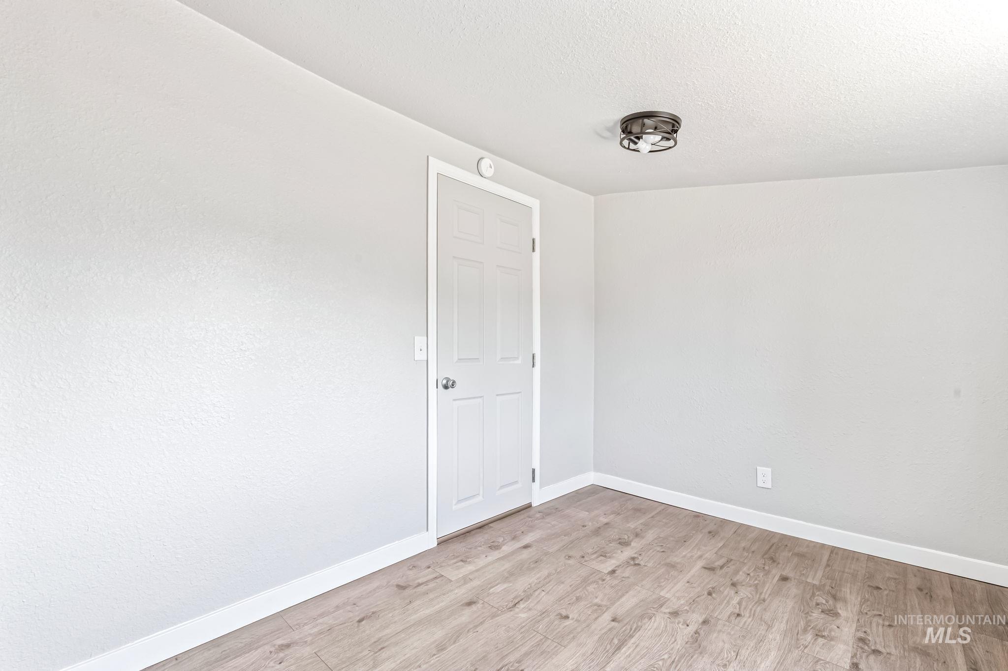 Unfurnished room featuring light wood finished floors, a textured ceiling, and a smoke detector