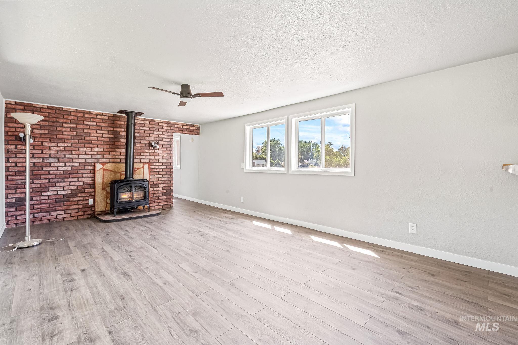 Unfurnished living room with ceiling fan, a wood stove, a textured ceiling, and wood finished floors