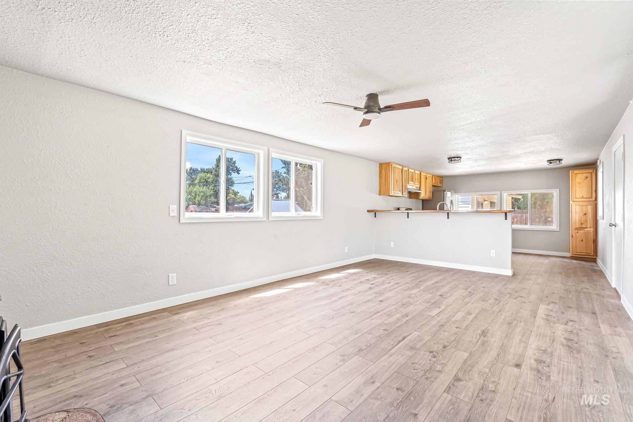 Unfurnished living room with ceiling fan, light wood-style floors, and a textured ceiling