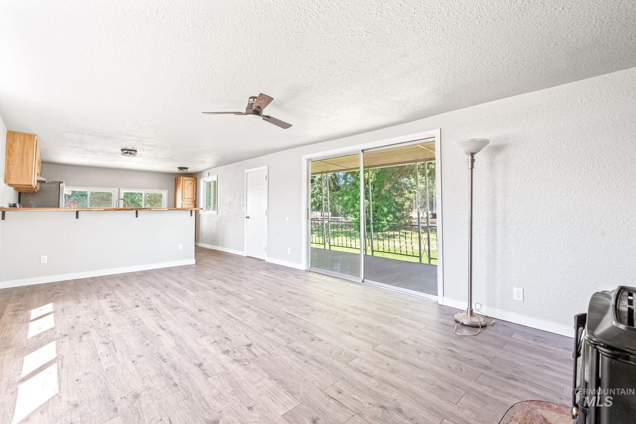 Unfurnished living room with light wood finished floors, plenty of natural light, a textured ceiling, and ceiling fan