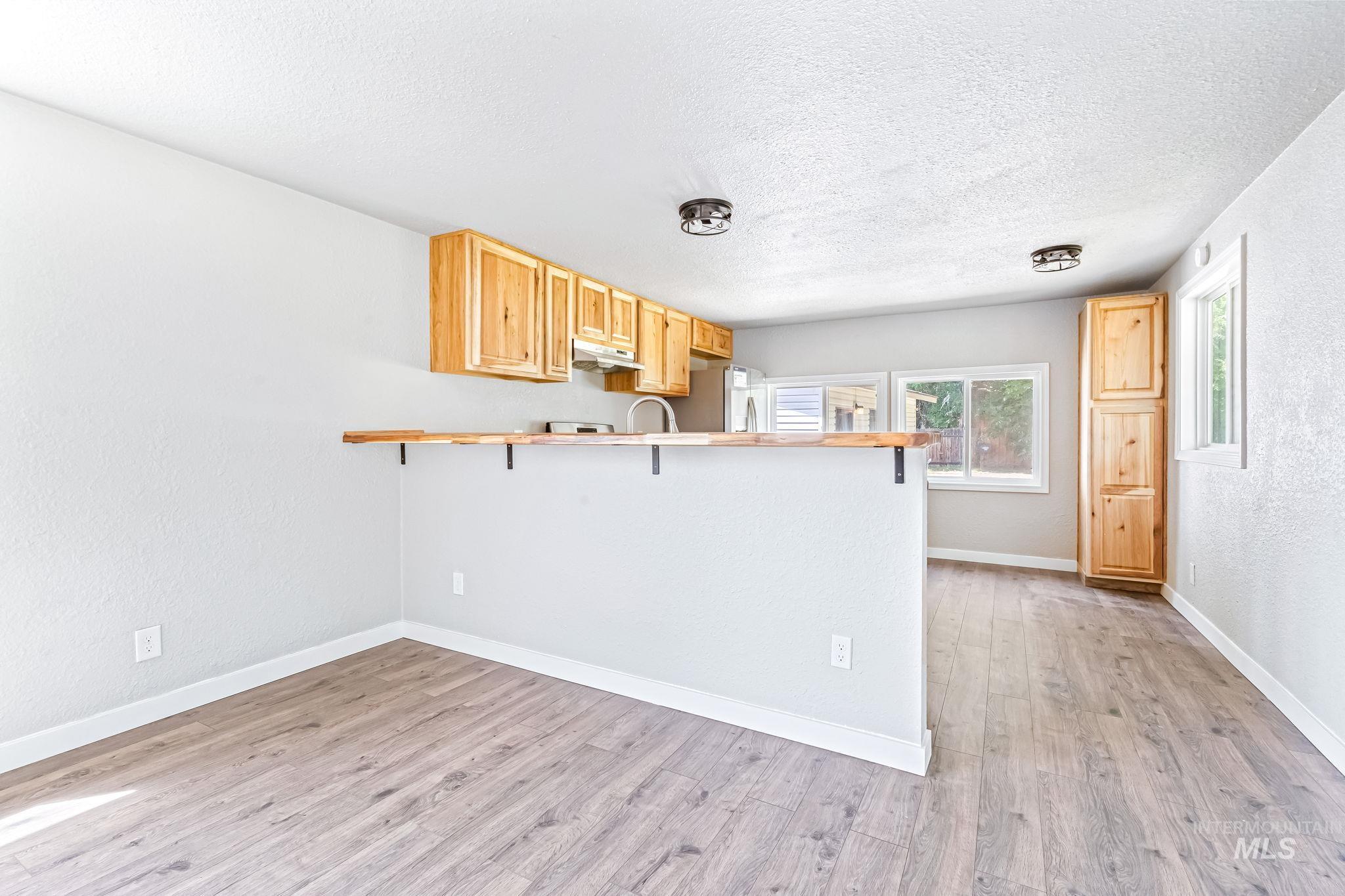 Kitchen featuring a textured ceiling, a peninsula, a kitchen bar, light wood finished floors, and under cabinet range hood