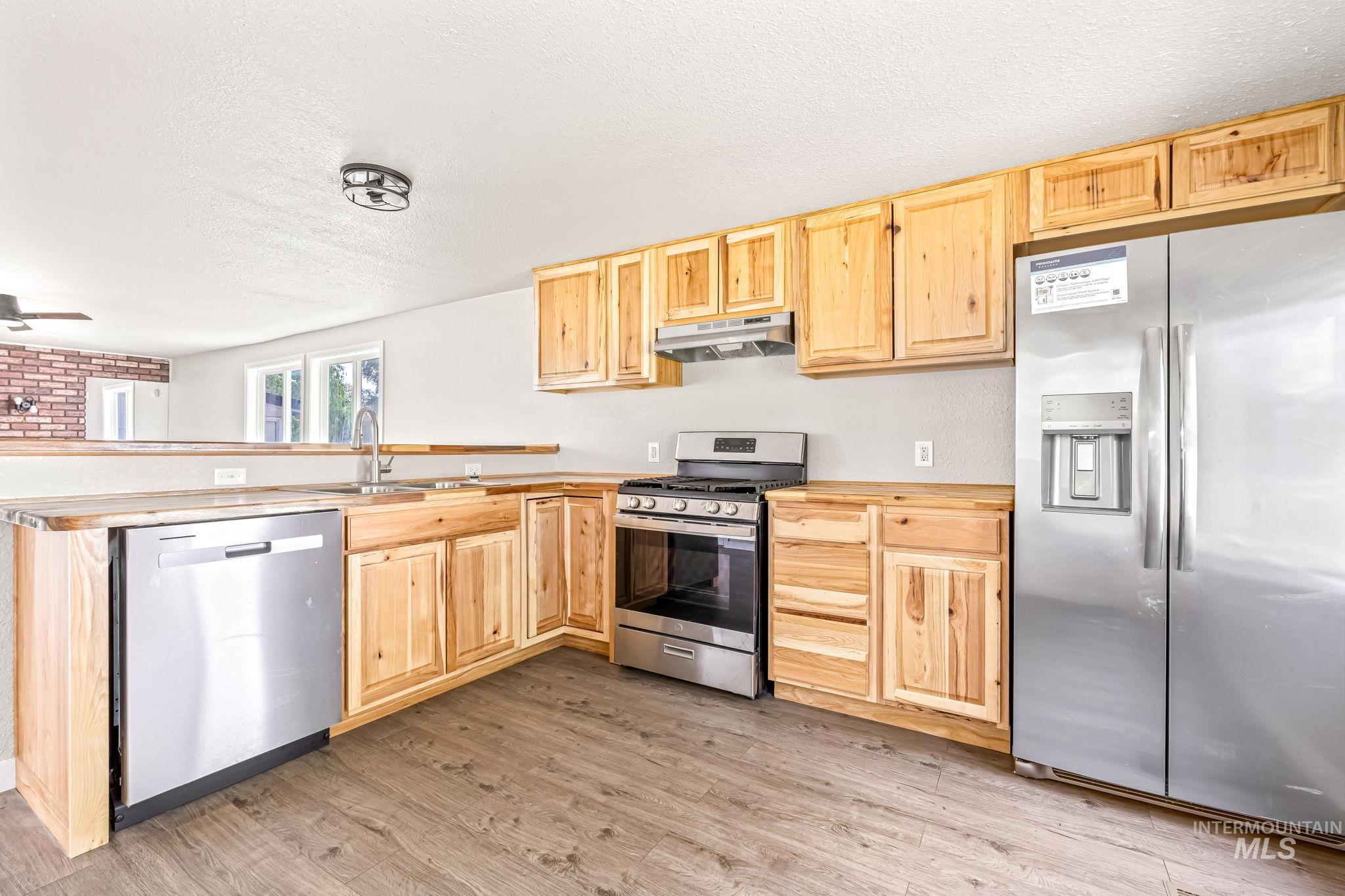 Kitchen with appliances with stainless steel finishes, under cabinet range hood, light brown cabinetry, a textured ceiling, and a peninsula