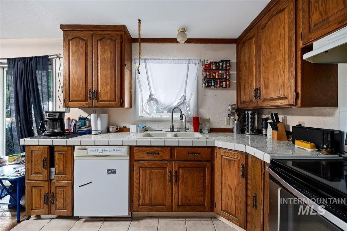 Kitchen featuring brown cabinets, white dishwasher, electric stove, tile counters, and light tile patterned floors