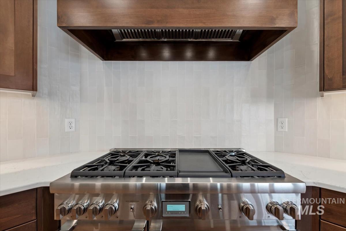 Kitchen featuring custom exhaust hood, decorative backsplash, gas stove, and light stone counters