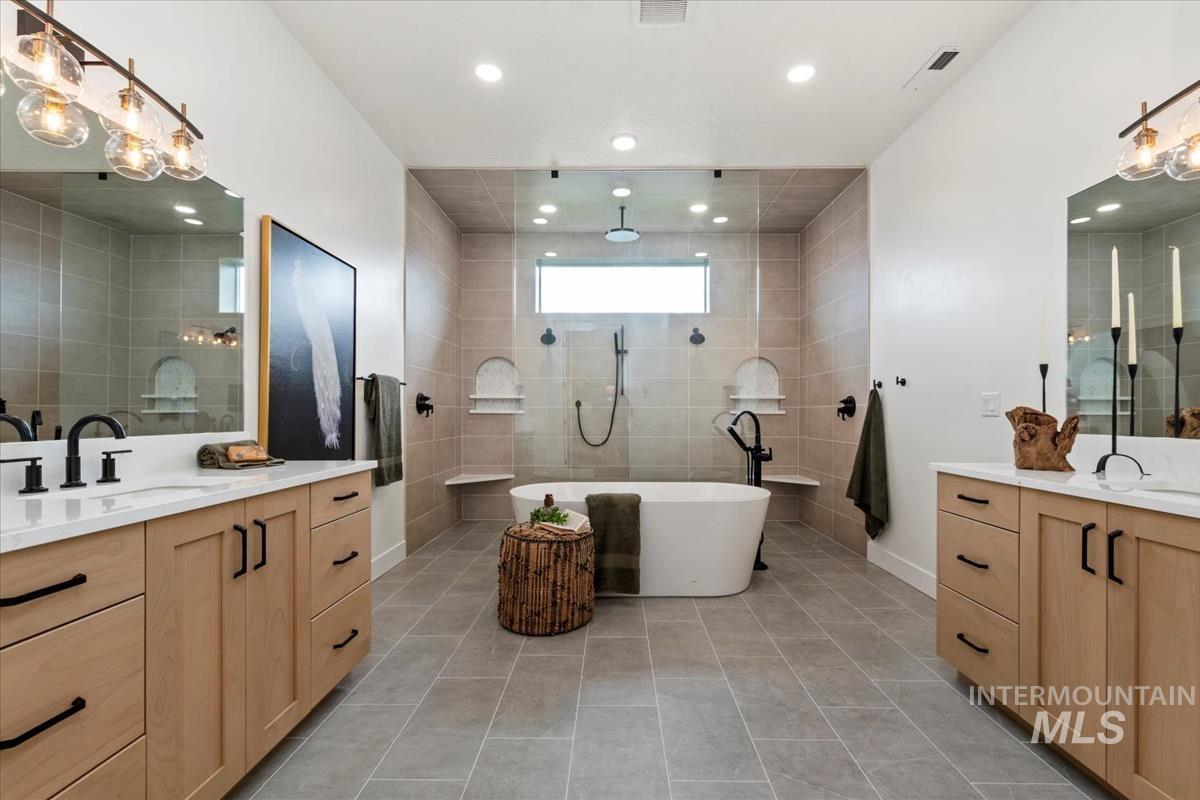 Full bathroom featuring two vanities, light tile patterned flooring, walk in shower, a freestanding bath, and recessed lighting