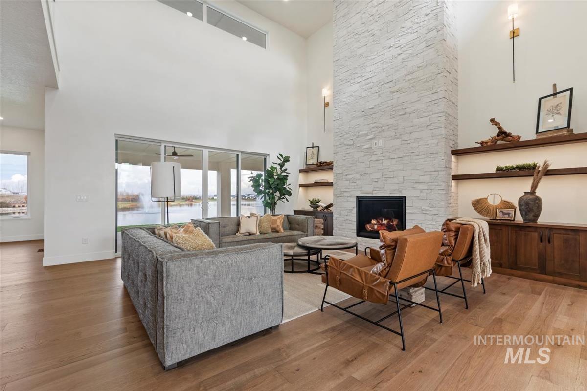 Living area with a high ceiling, a stone fireplace, light wood finished floors, and plenty of natural light