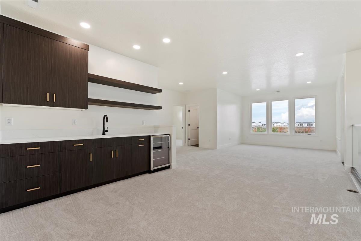 Bar area with open shelves, dark brown cabinetry, light countertops, wine cooler, and light colored carpet