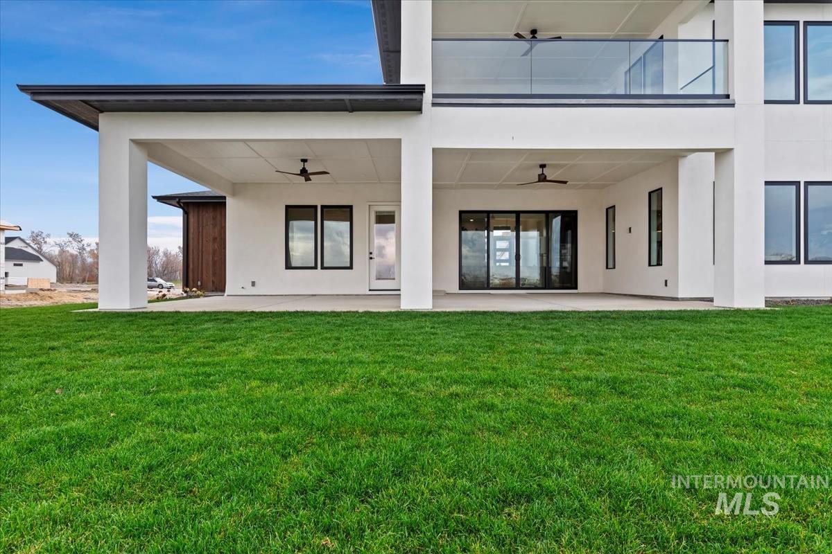 Back of property with ceiling fan, stucco siding, and a lawn
