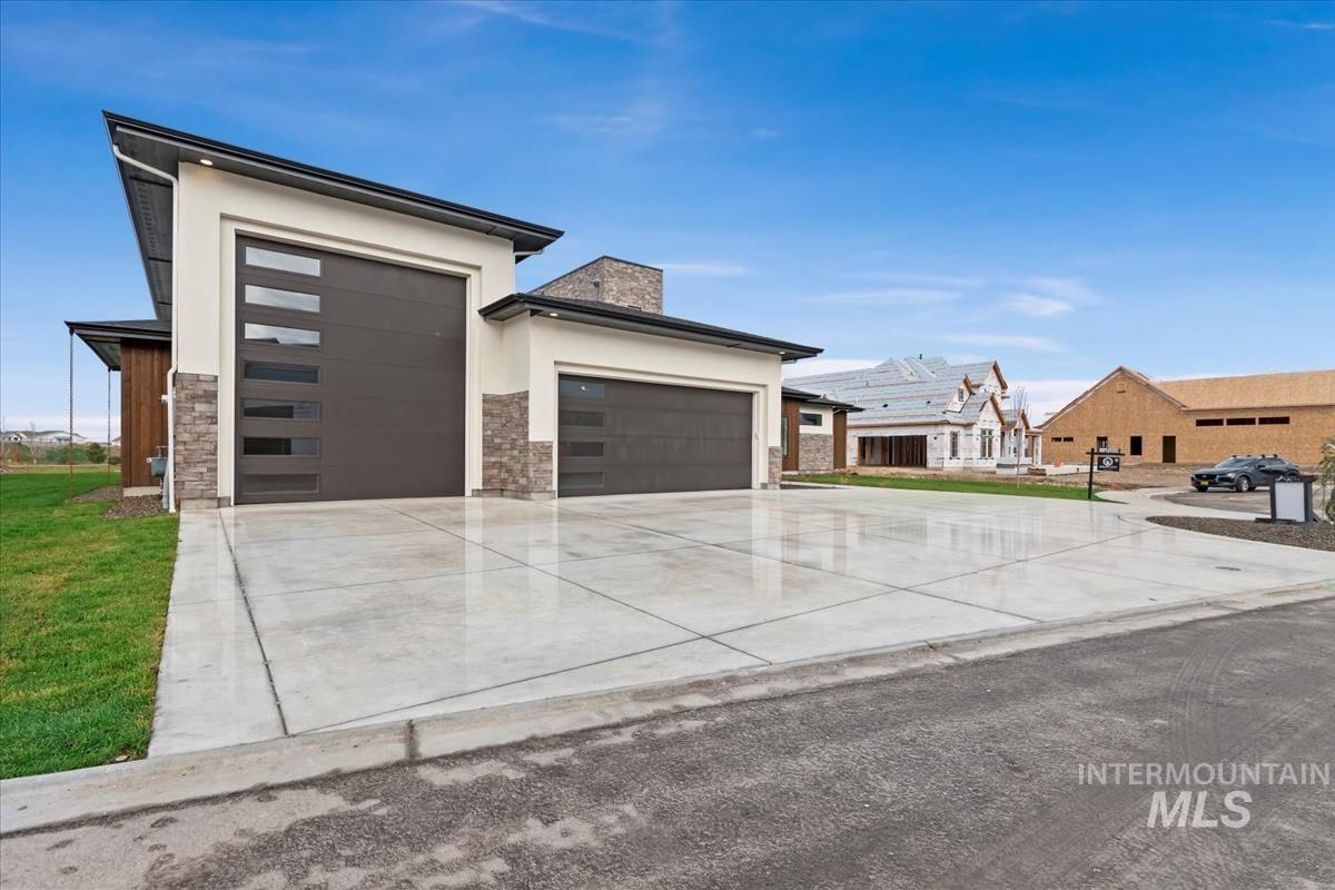 View of front of property featuring a garage, driveway, stone siding, a chimney, and stucco siding
