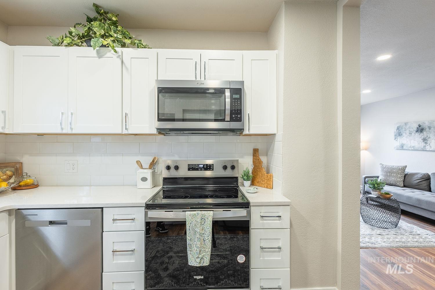 Kitchen with appliances with stainless steel finishes, white cabinetry, backsplash, wood finished floors, and light stone counters